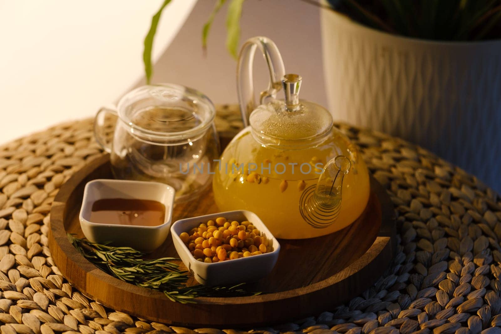 A teapot with sea buckthorn tea, honey and a plate with sea buckthorn on a tray.