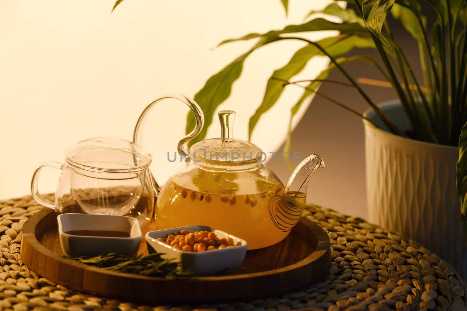 A teapot with sea buckthorn tea, honey and a plate with sea buckthorn on a tray by Lobachad