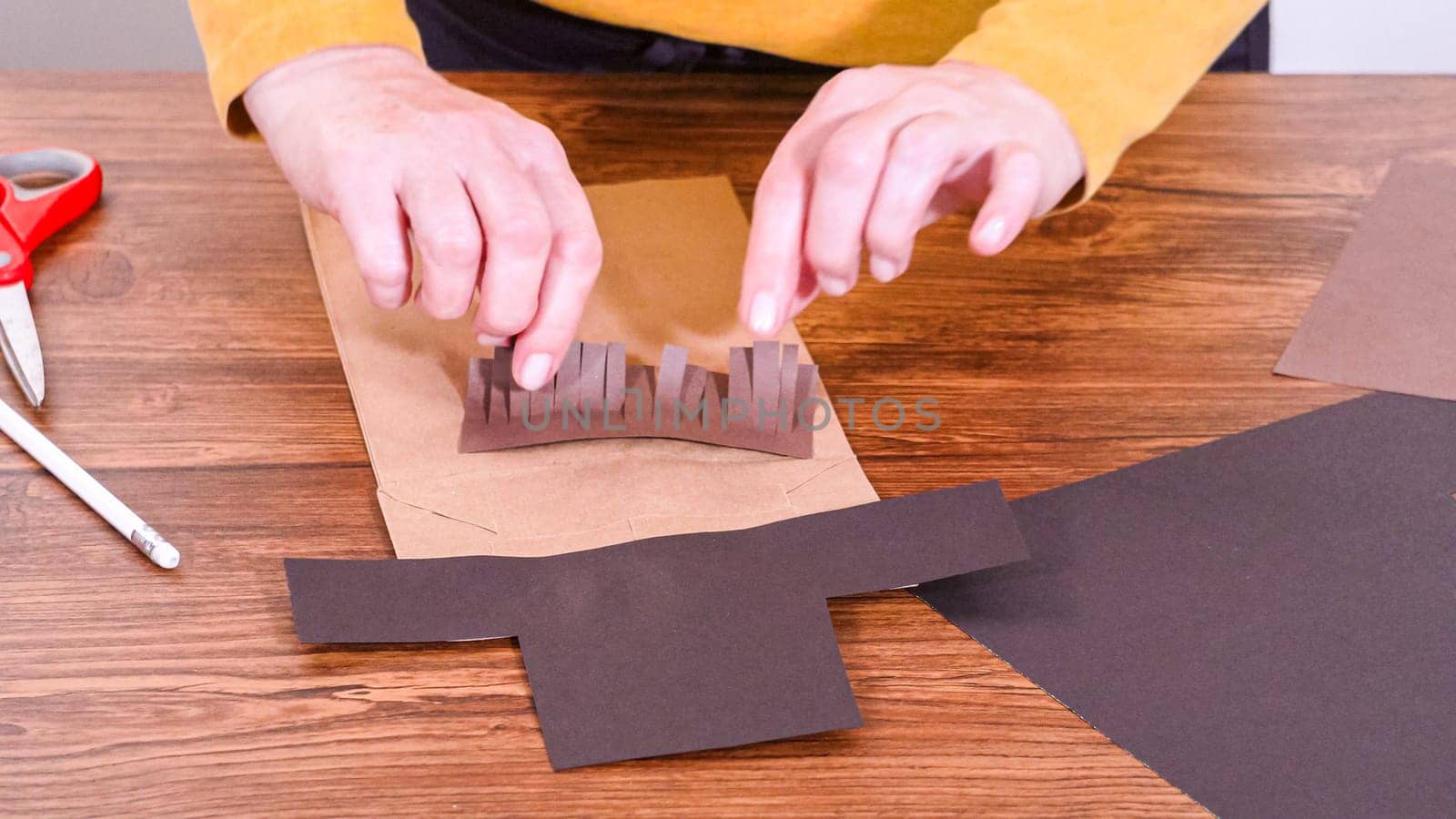 Step by step. Teacher guides online class through making a paper puppet from a brown bag, creatively using a wooden surface as a workspace.