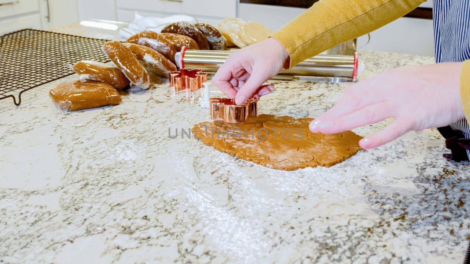 Using various festive cookie cutters, we're cutting out charming gingerbread cookies from the rolled dough on the sleek marble counter, bringing holiday cheer to the modern kitchen.