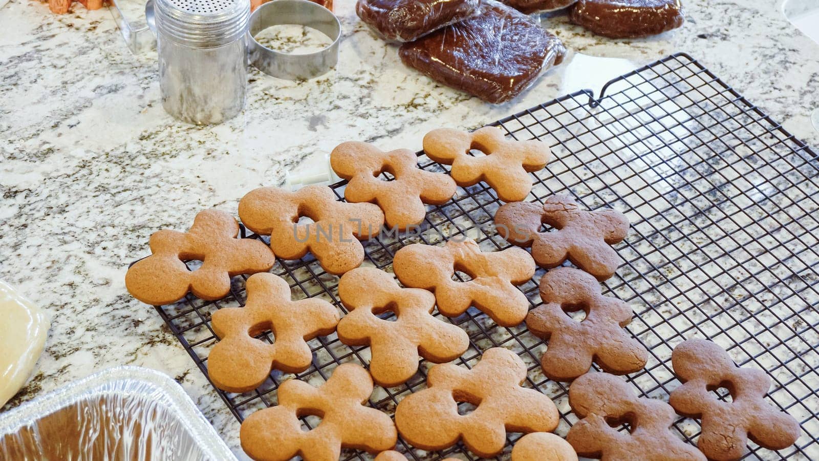 After baking to perfection, these delightful gingerbread cookies are now cooling gracefully on a wire rack, filling the modern kitchen with a warm and inviting aroma.