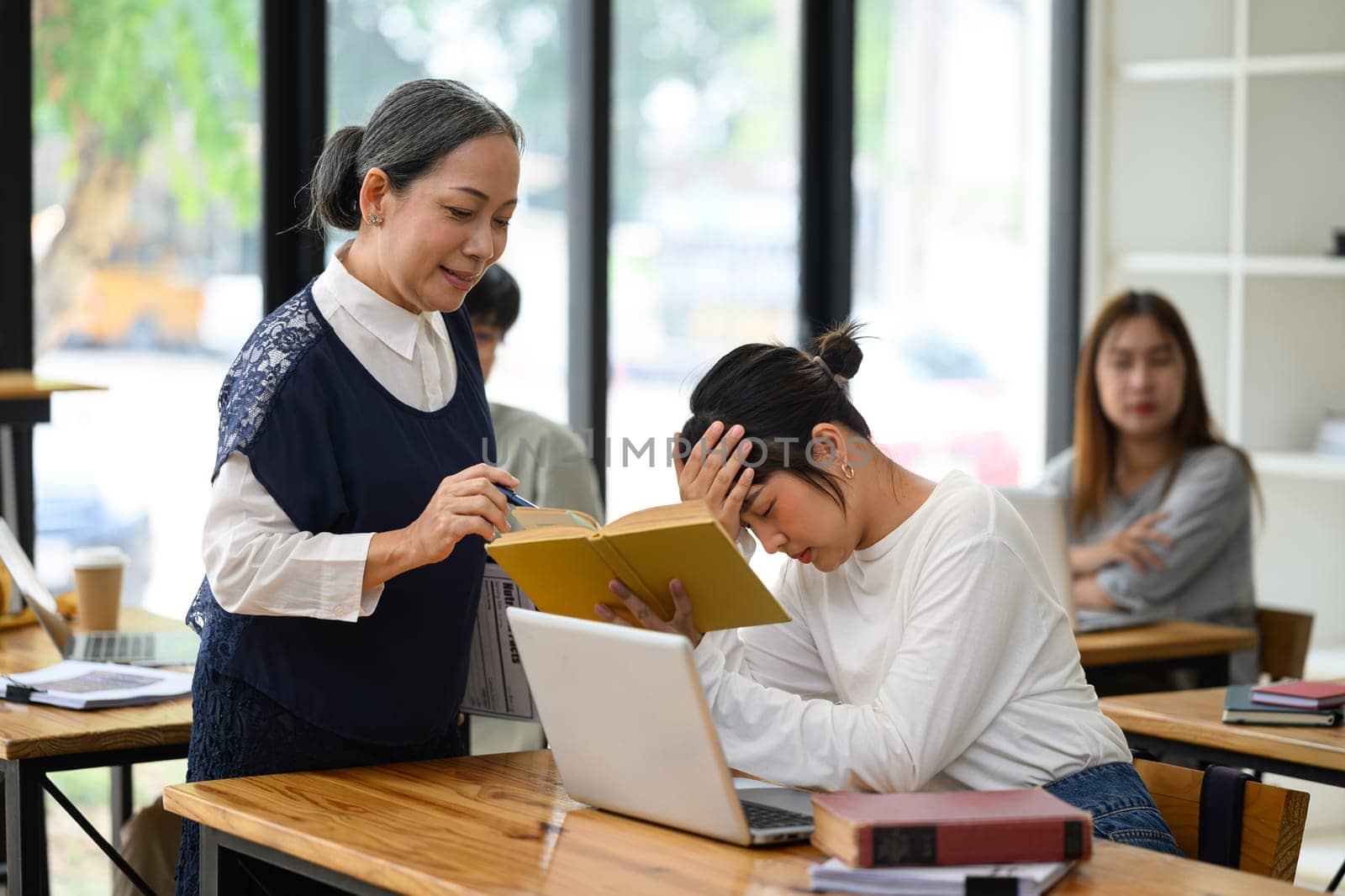 Middle age teacher assisting a struggling student with assignment in a classroom.