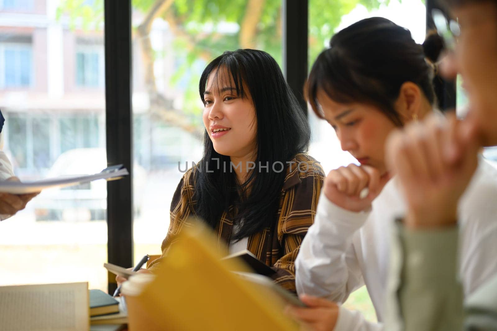 Group of college students sitting at desk learning together in library by prathanchorruangsak
