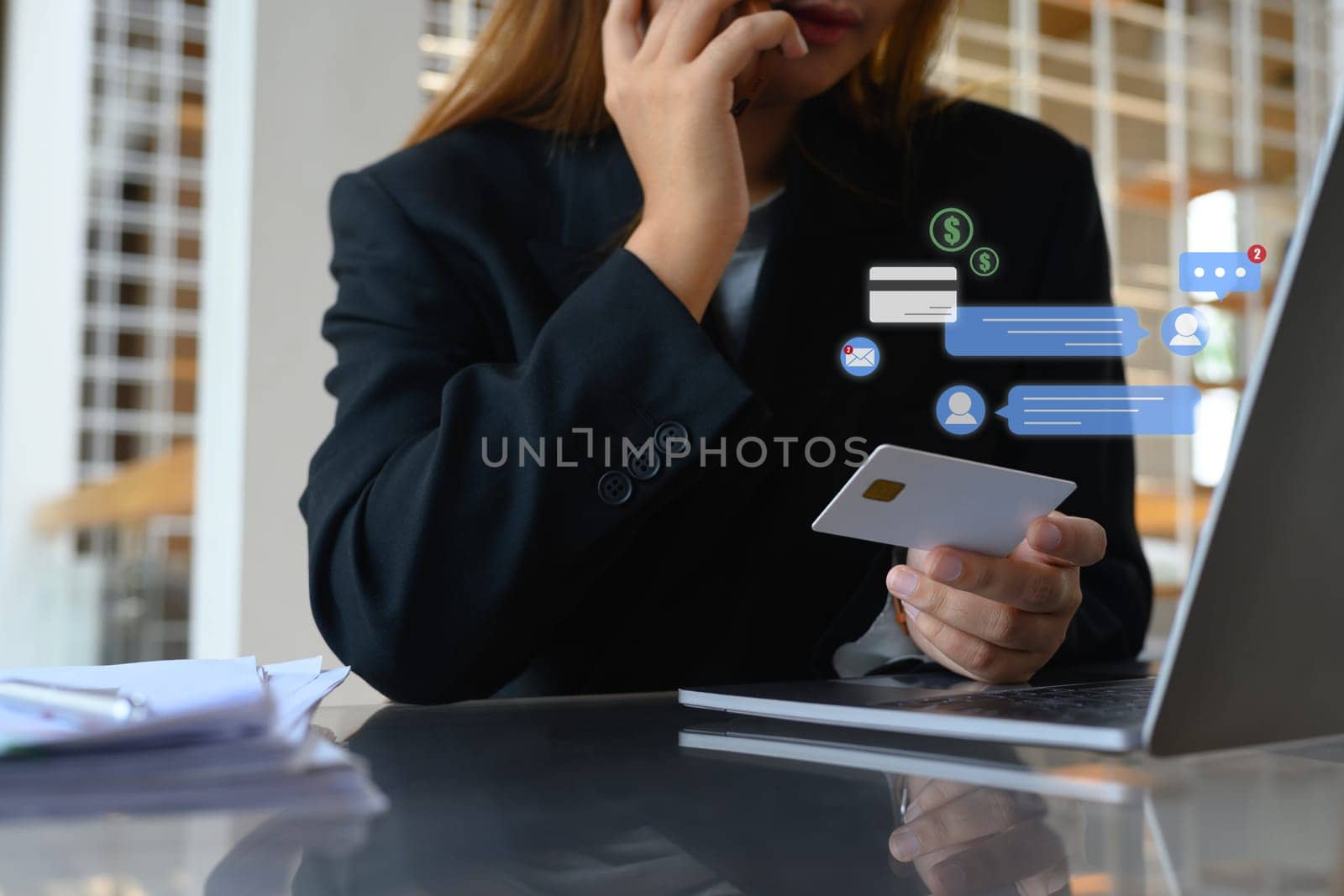 Businesswoman with a credit card in hand talking on mobile phone at her office desk by prathanchorruangsak
