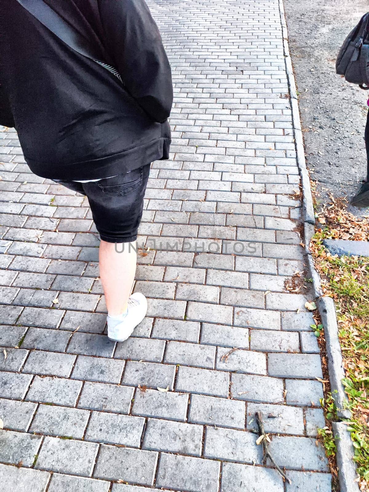 Person walking on a brick-laid path in the evening. Casual Stroll on Cobblestone Sidewalk at Dusk by keleny