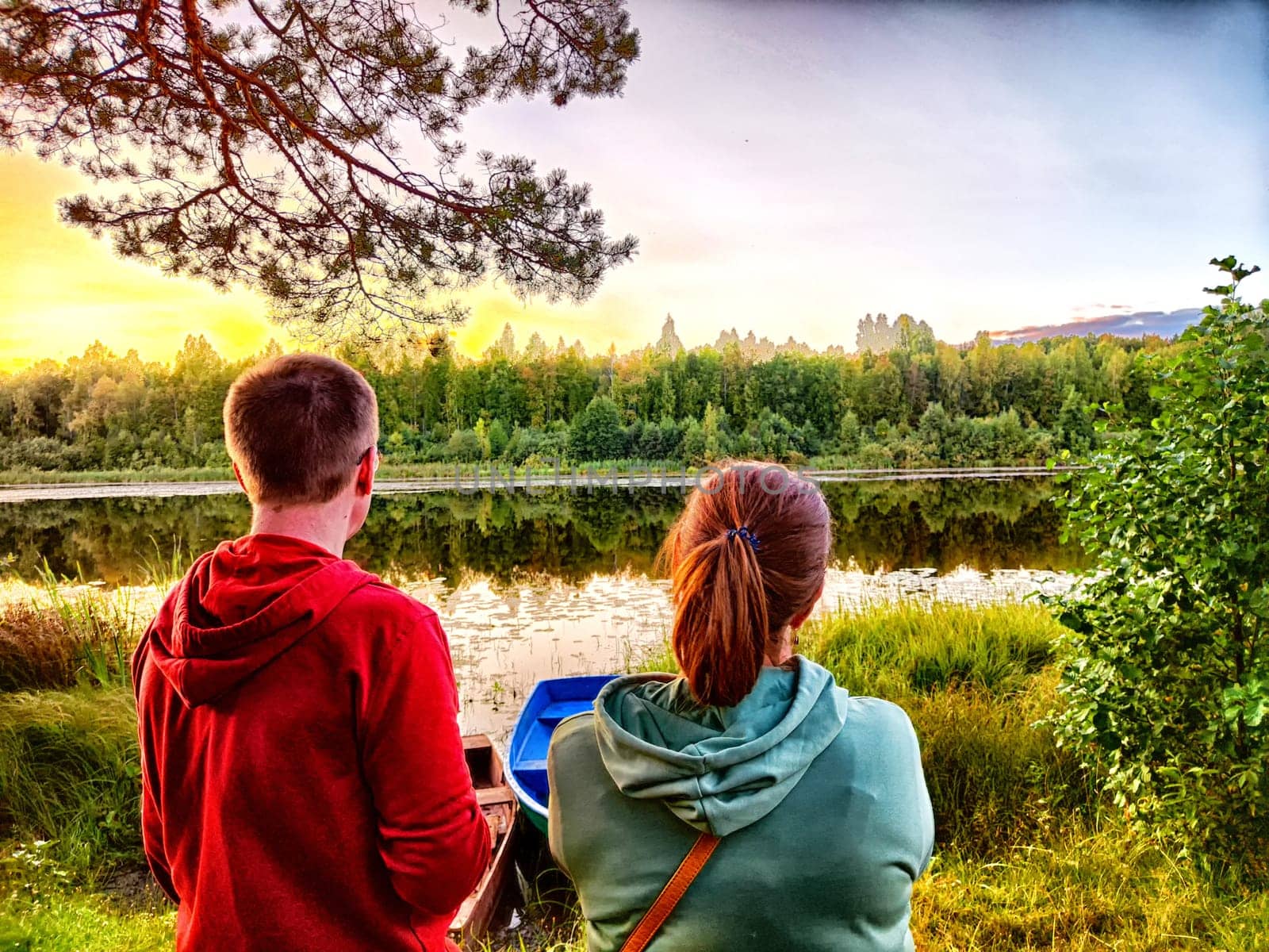 Tourist Couple Enjoying a Lakeside Sunset in Nature. A couple watches the sunset by a tranquil lake, surrounded by trees by keleny