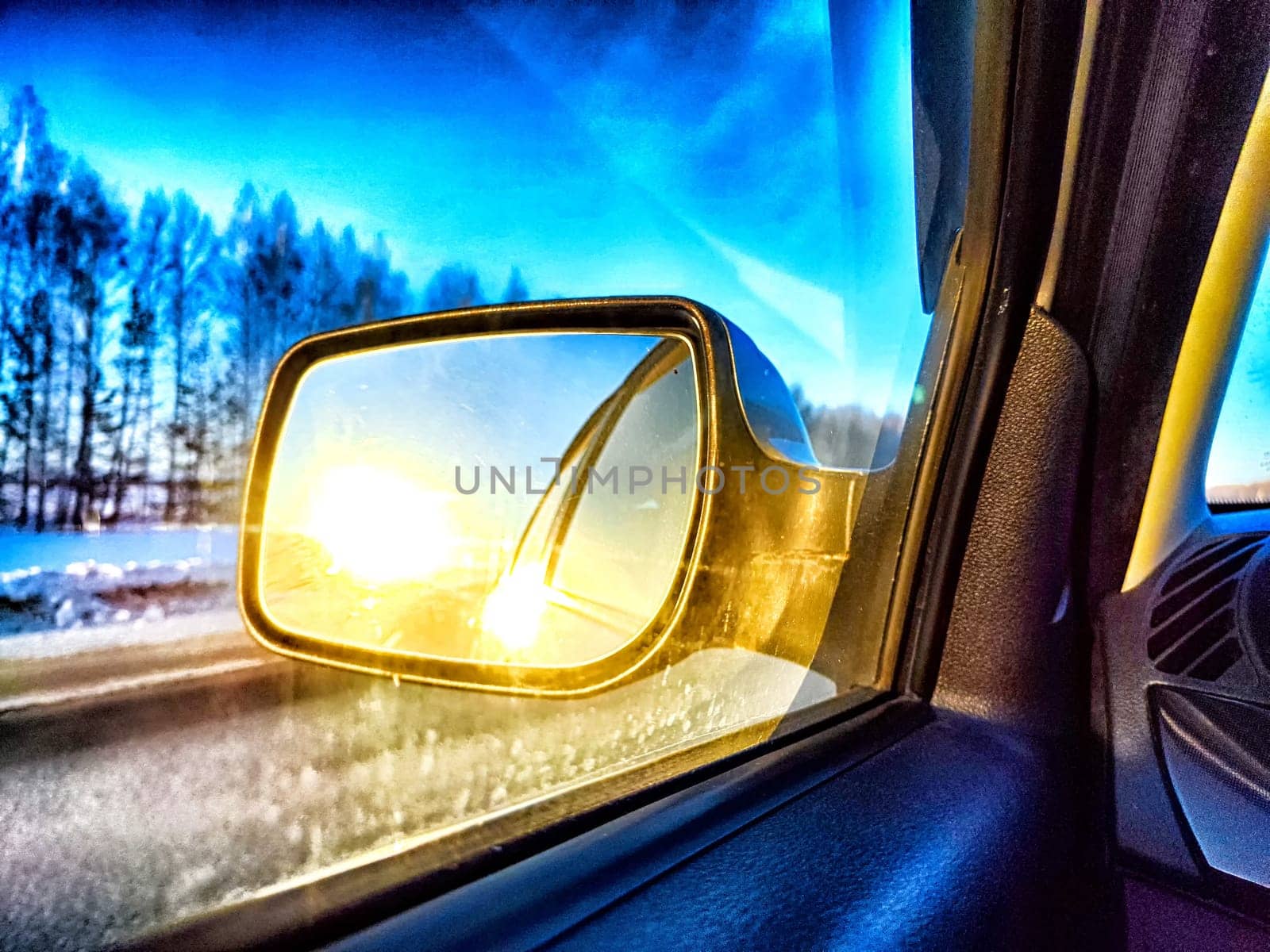 The side mirror of the car and the sun with bright rays in it and the track on a trip in nature by keleny