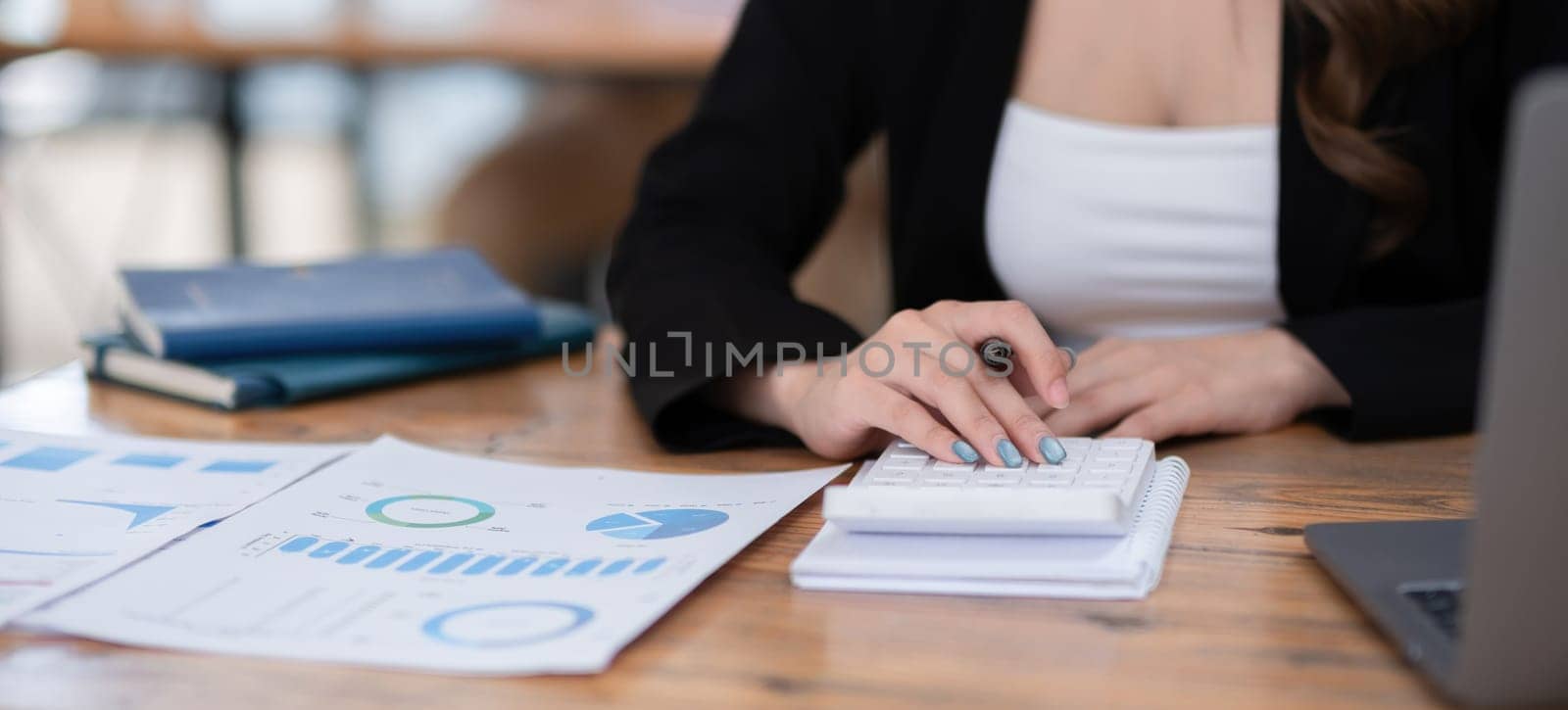 Beautiful accountant sitting with laptop calculating financial and tax figures for company on table in office room by wichayada
