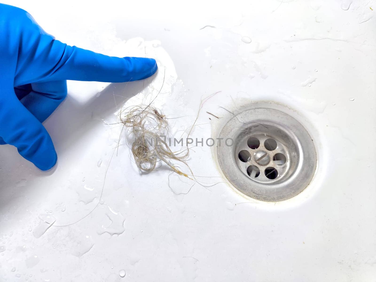 Removing Hair Clog From a Bathroom Sink Drain. Gloved hand extracting hair from sink