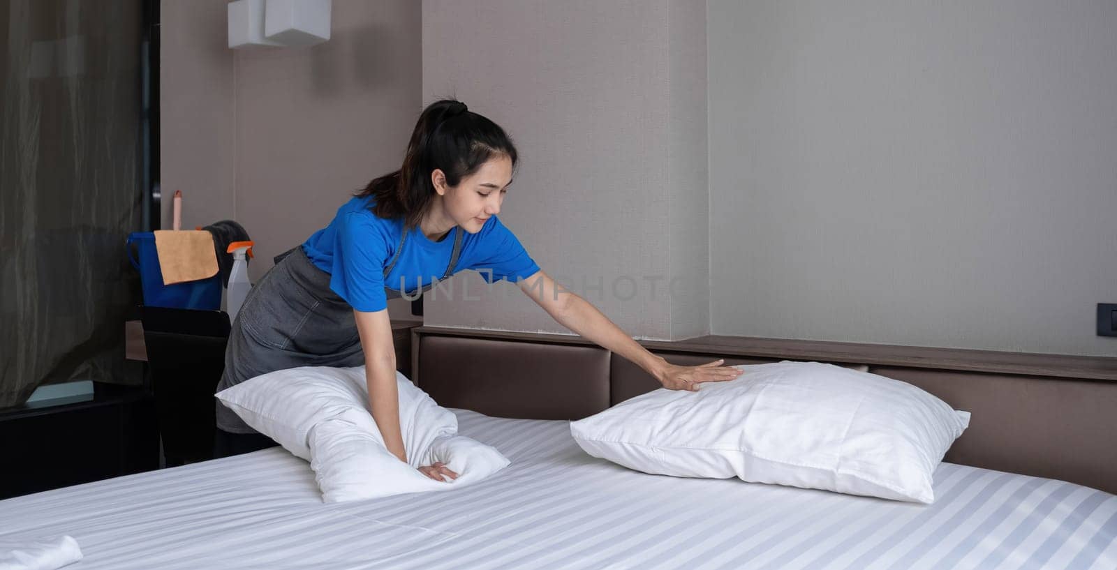 The hotel housekeeper in the room was cleaning the bed and preparing the bedding..
