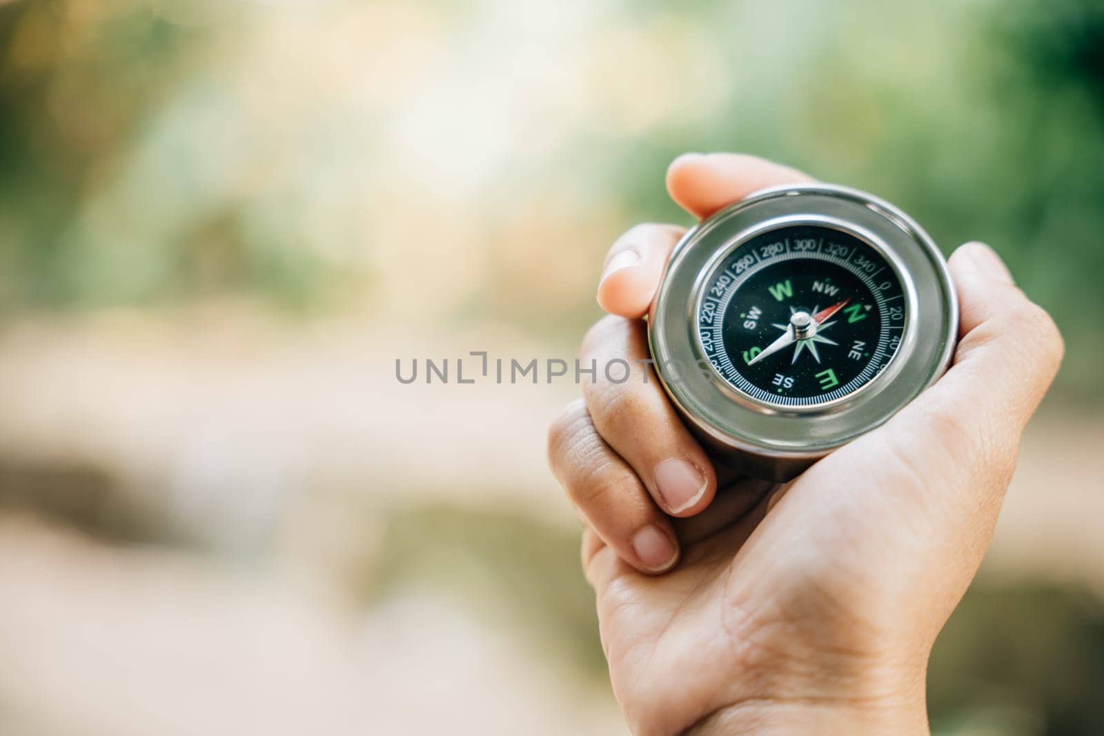 A traveler holding a compass in a park seeks guidance and direction in nature beauty. The compass in the woman hand signifies exploration and a journey to find one path.
