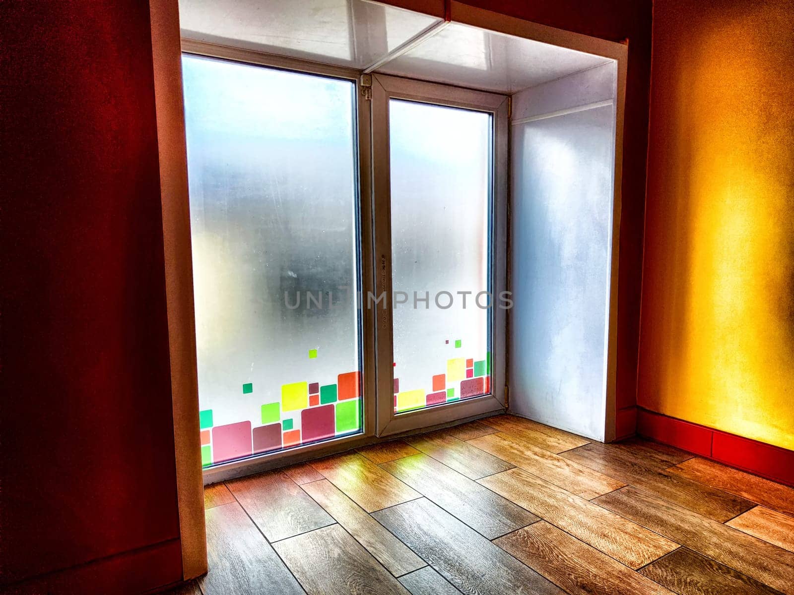 Window and floor. Background, texture. A frosted glass door adorned with vibrant squares allows diffused light into a room with wooden floors