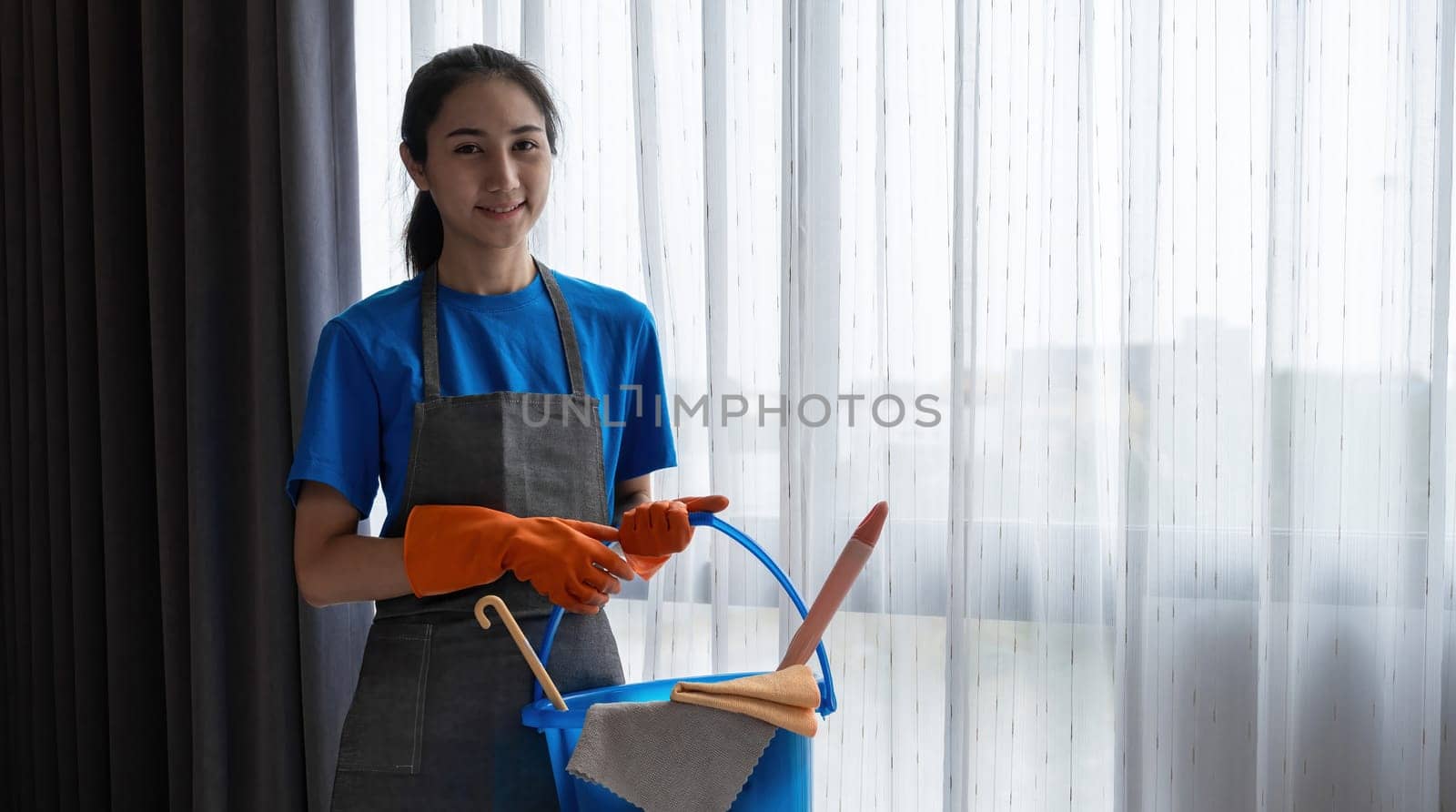 A young female cleaning lady stands holding cleaning tools and prepares to clean the floor..