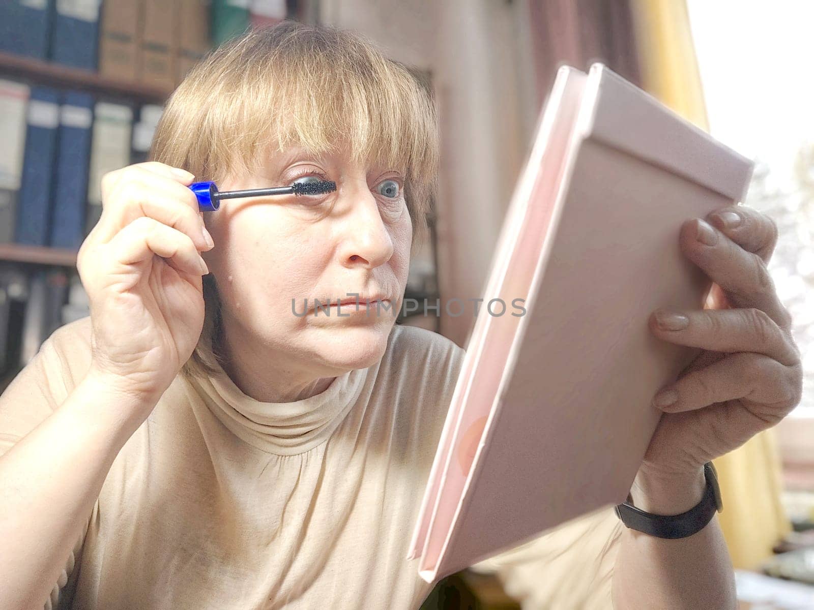Portrait of a middle-aged woman doing eye makeup. Selfie portrait of lady who is businesswoman, accountant, manager, freelancer doing morning makeup at office on working place
