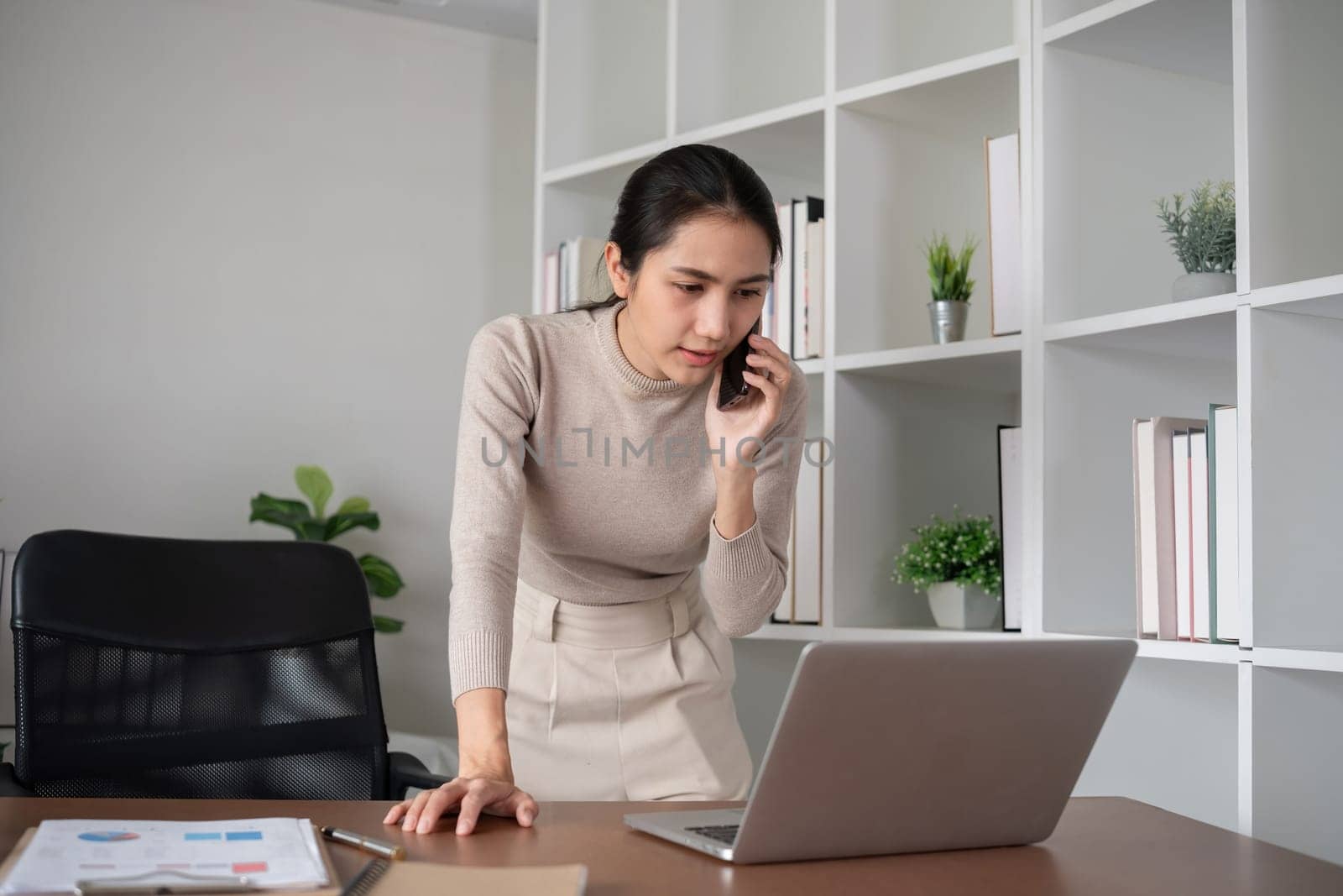 Asian businesswoman talking on the phone, having an online business meeting in a modern home office. by wichayada