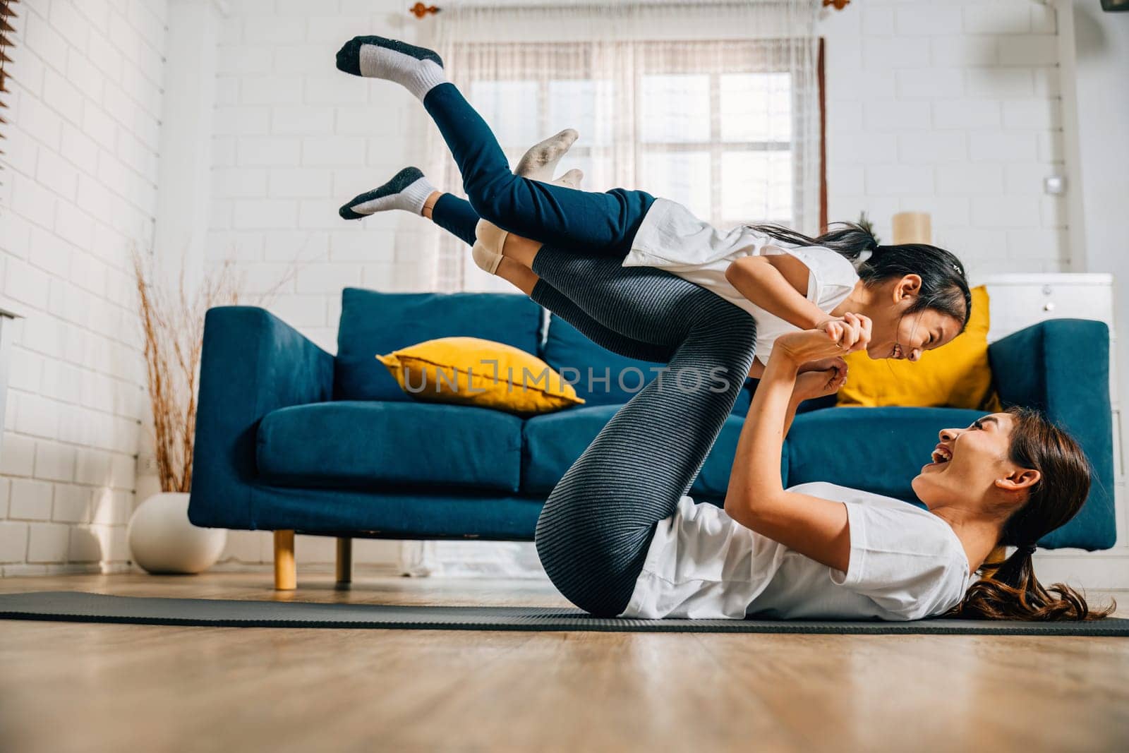 A harmonious family practices the little bird posture in yoga at home by Sorapop