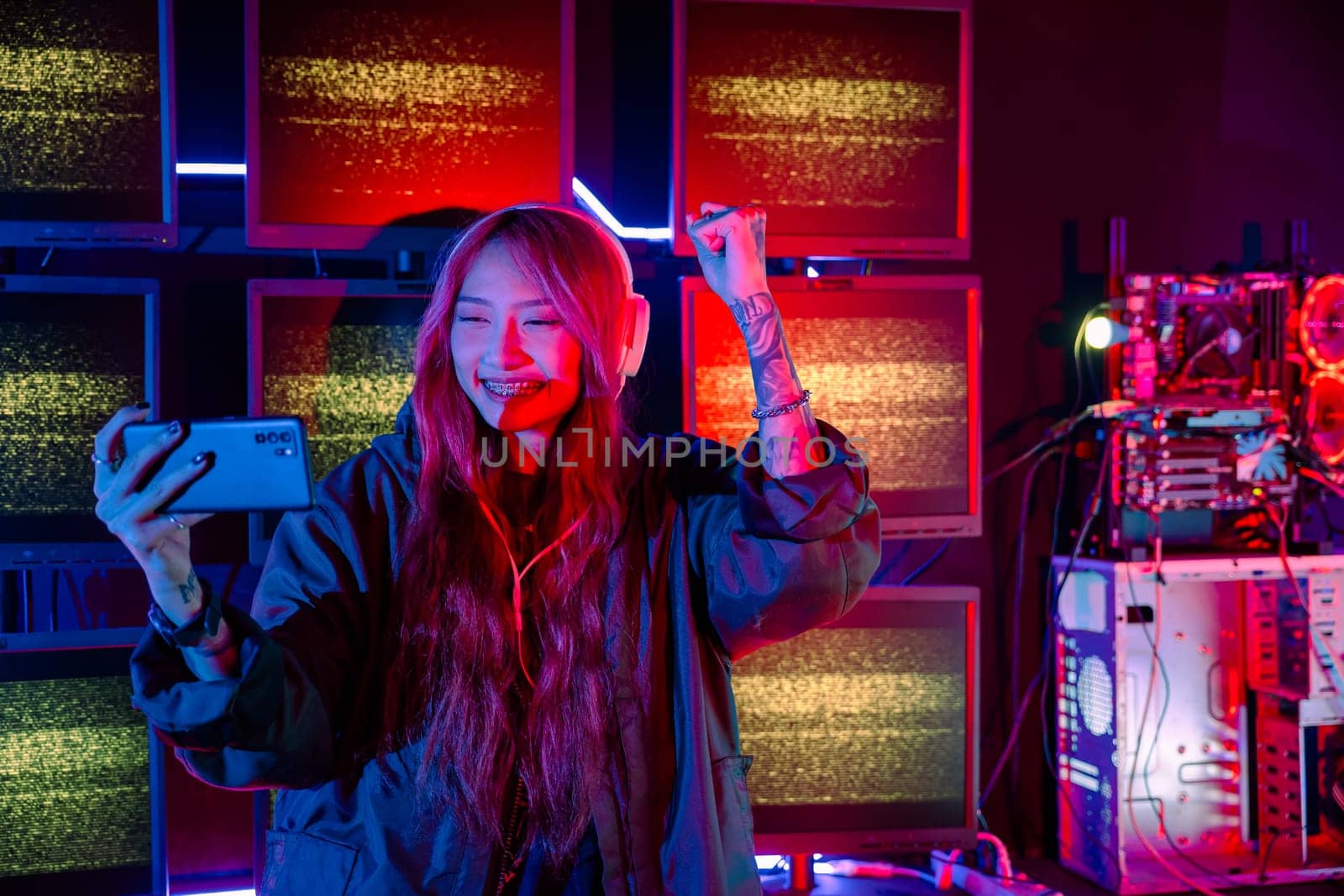 Winning. Young woman feeling excited at gaming room, Happy gamer people playing video game online with smart mobile phone with neon lights raising hands to wins celebrating, smile with smartphone
