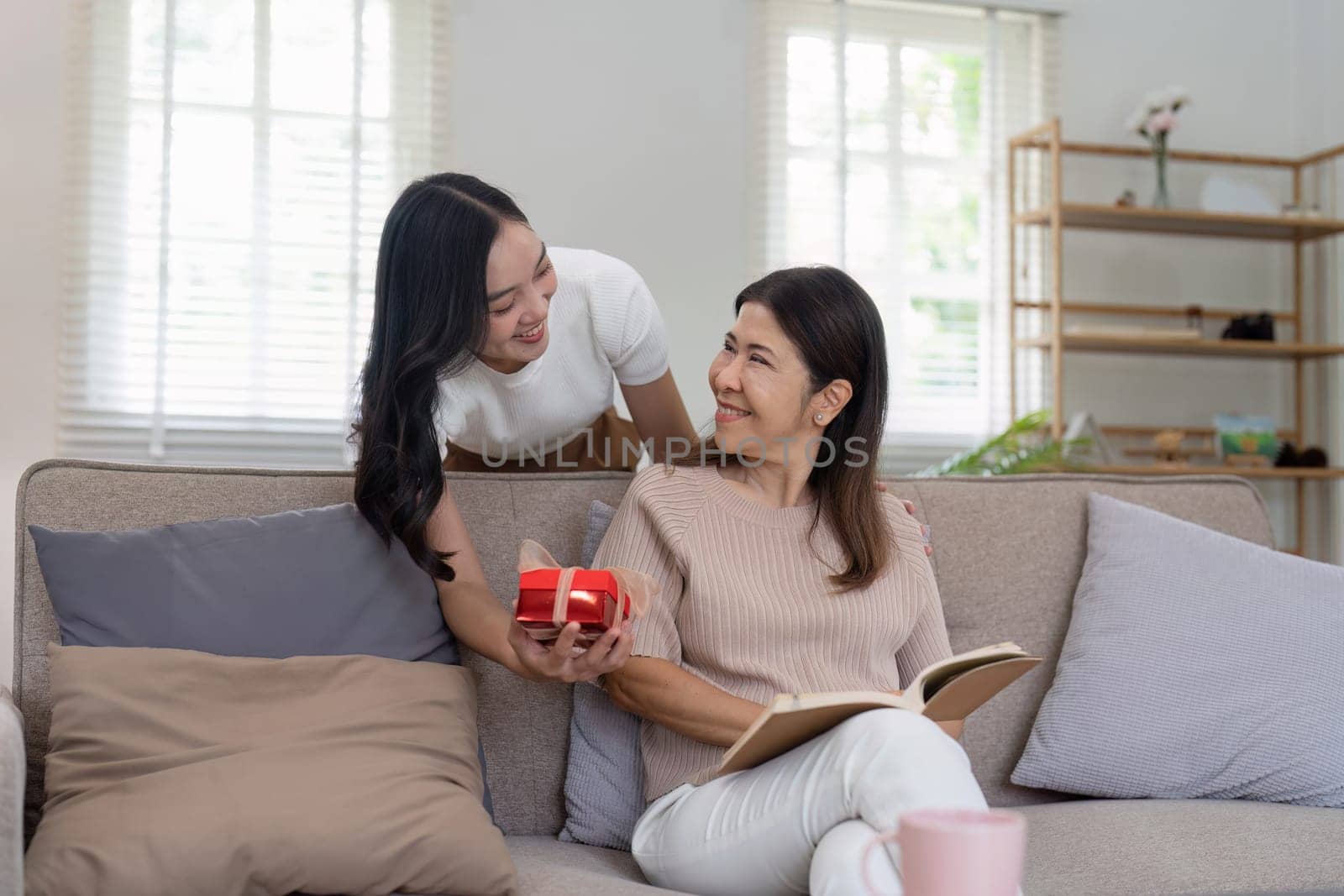 Congratulations. Loving asian mature daughter surprised mother with present in Mother's Day, giving her handmade card and gift box.