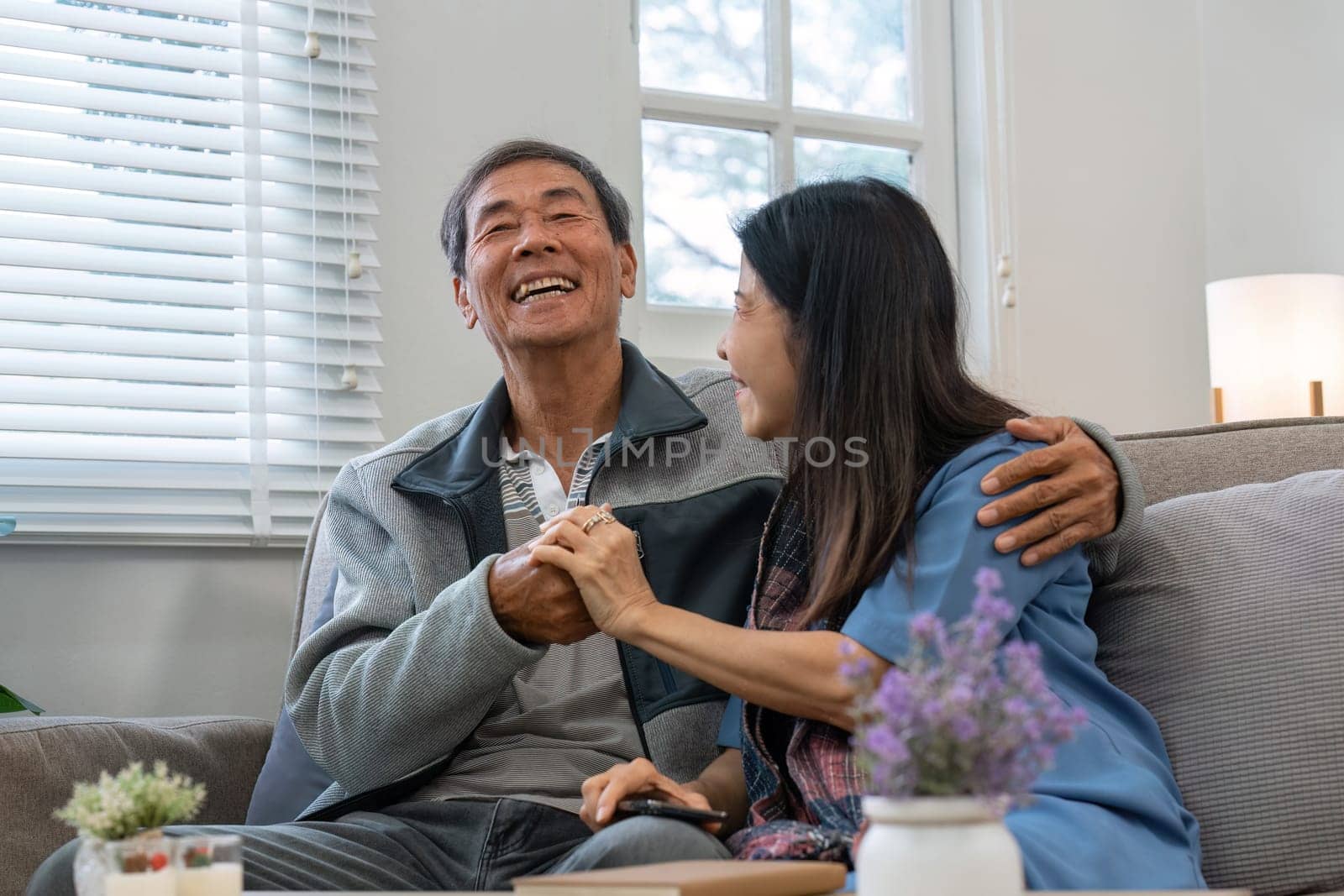 A man and woman are sitting on a couch, the man is holding the woman's hand. Scene is warm and affectionate
