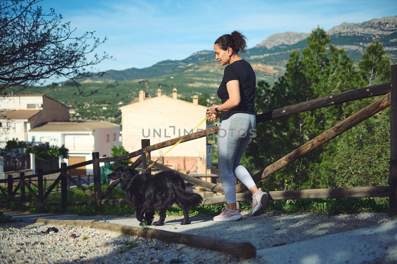 Young happy active woman in sports clothes, taking her dog for a walk while jogging on the morning in mountains nature on a warm sunny day. People. Sport. Domestic animals. Healthy active lifestyle