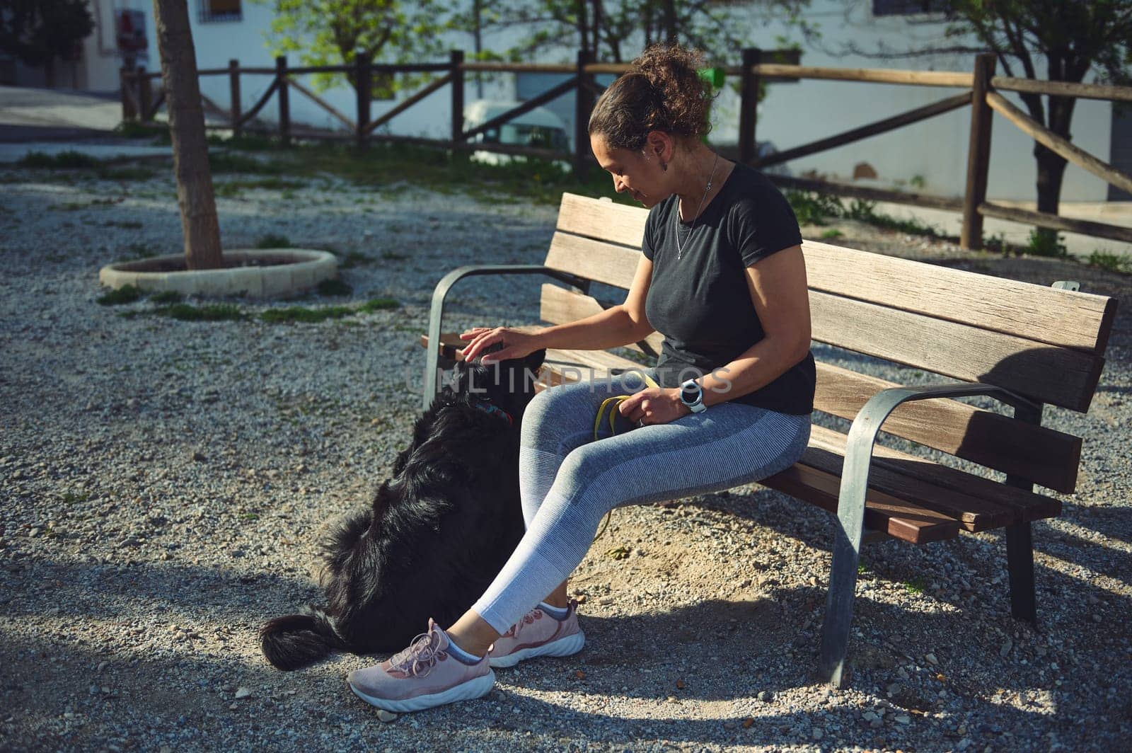 Happy young woman stroking her dog being walked on leach on the nature by artgf