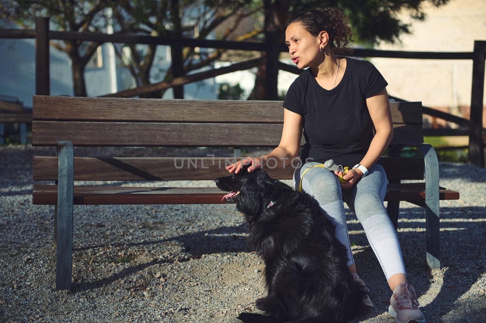 Authentic portrait of a pretty woman ang her pet, a black cocker spaniel on the bench on the nature outdoors. Woman walking dog in the summer park
