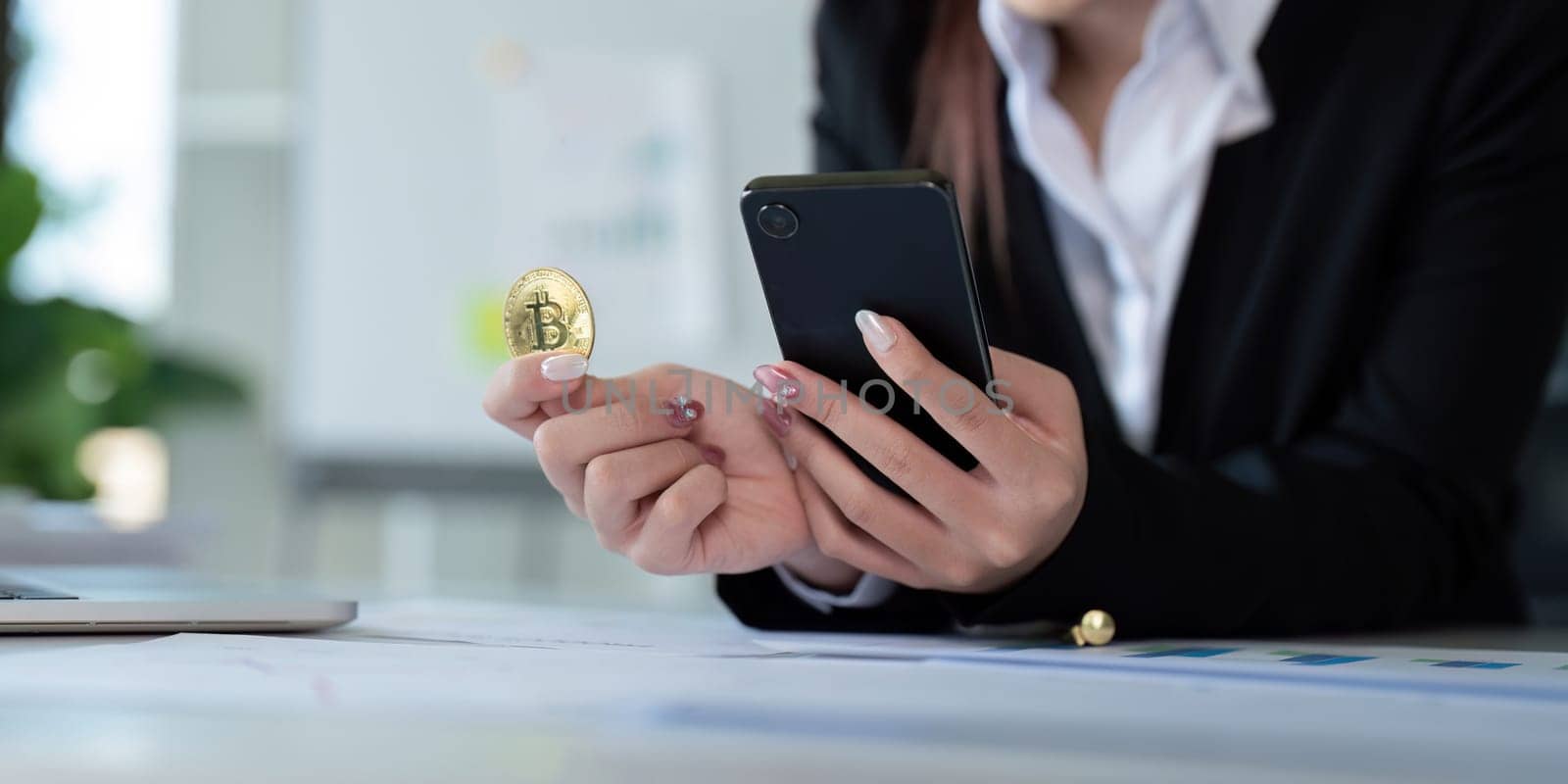 Businesswoman holding a golden bitcoin. using Mobile with graph chart, trading stock market, investing Bitcoin cryptocurrency at home office. Investment and technology concept by nateemee
