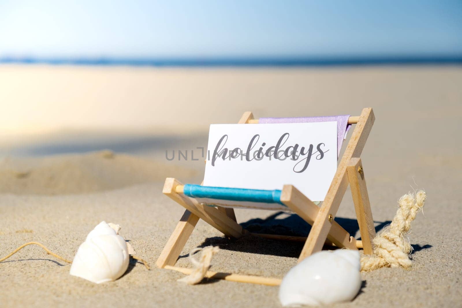 HOLIDAYS text on paper greeting card on background of beach chair lounge summer vacation decor. Sandy beach sun. Holiday concept postcard. Travel Business concept