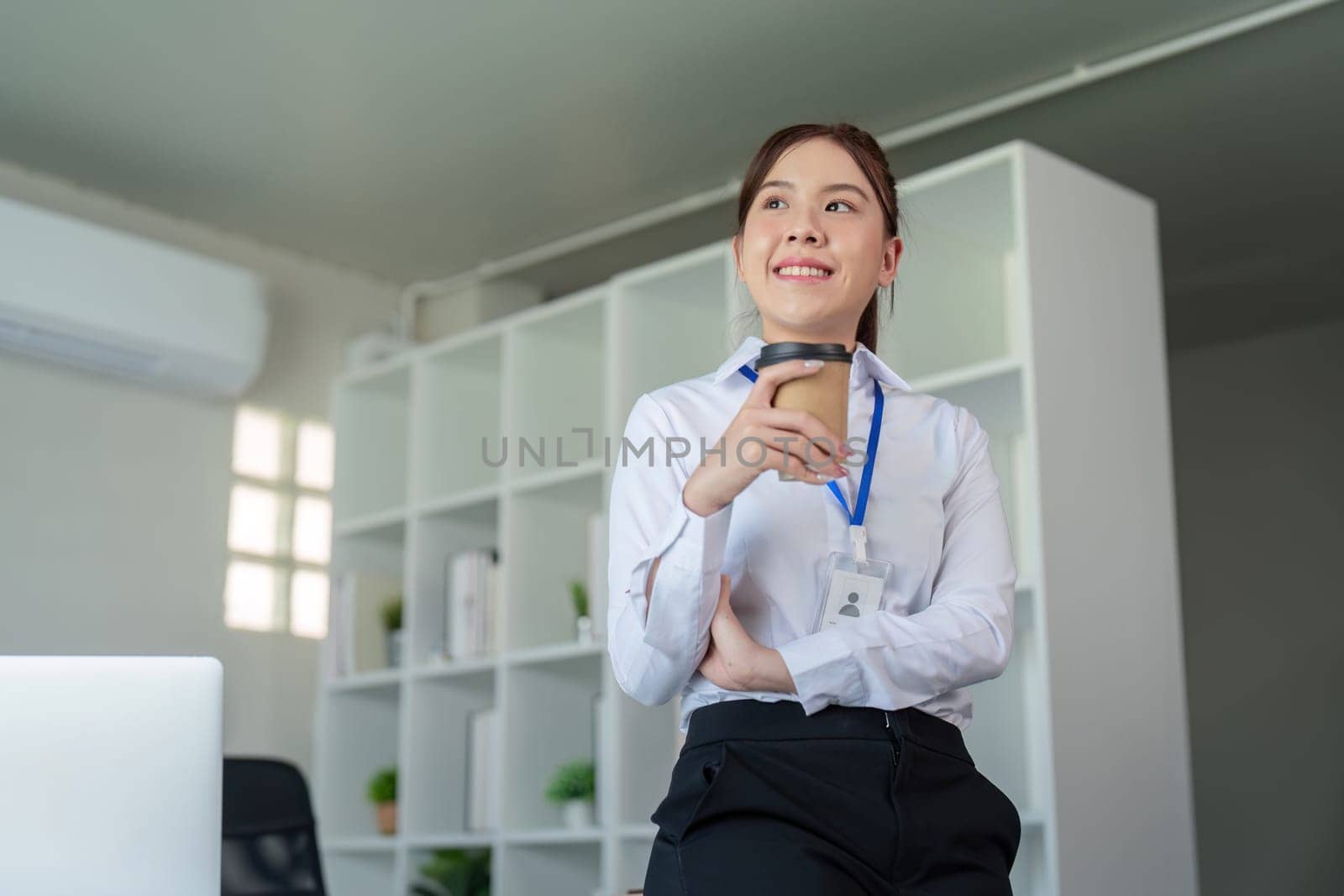 Young professional business woman, female company worker or manager holding coffee cup standing in corporate office.
