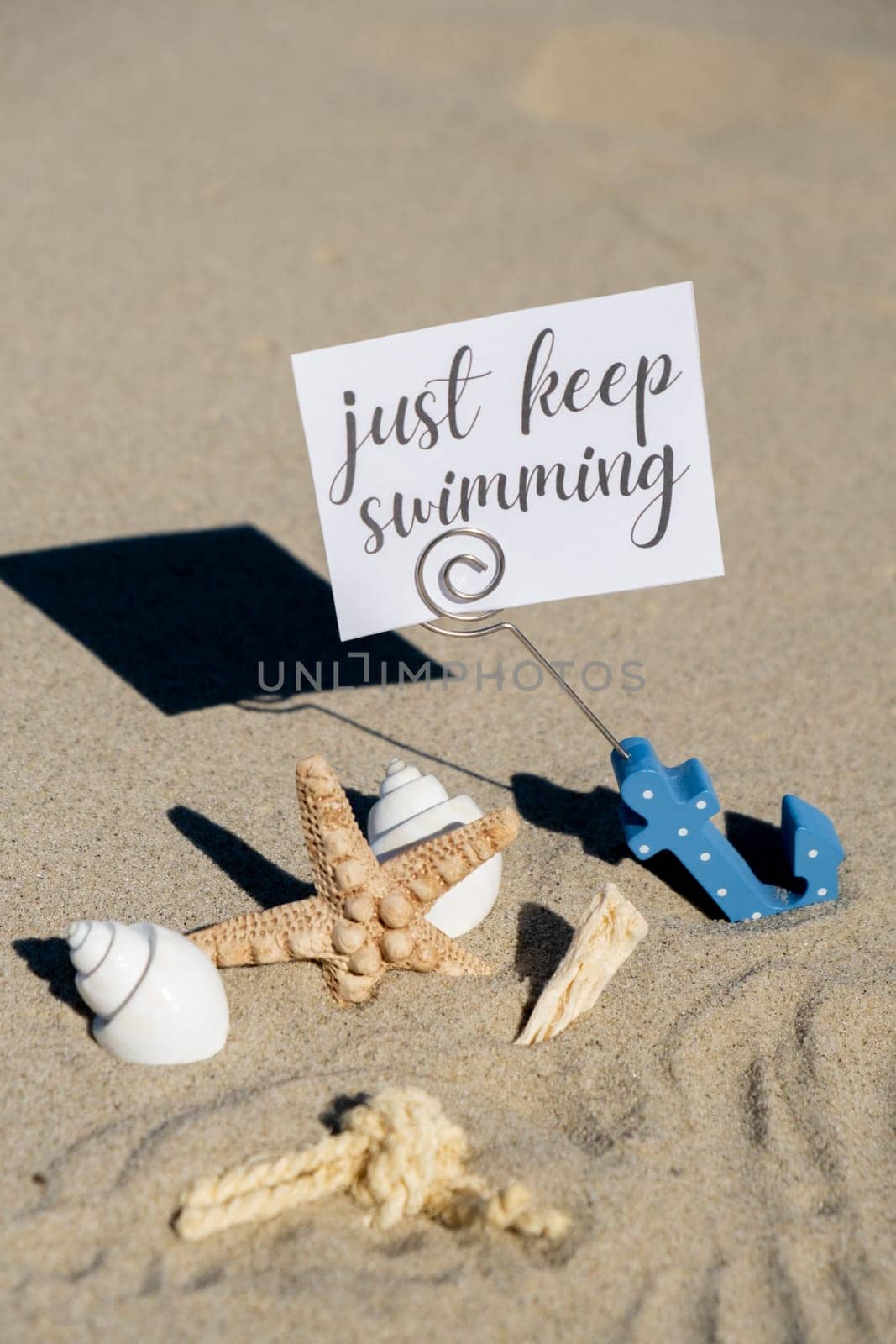 JUST KEEP SWIMMING text on paper greeting card in anchor paper holder and starfish seashell summer vacation decor. Sandy beach sun coast. Holiday concept postcard. Getting away Travel Business concept