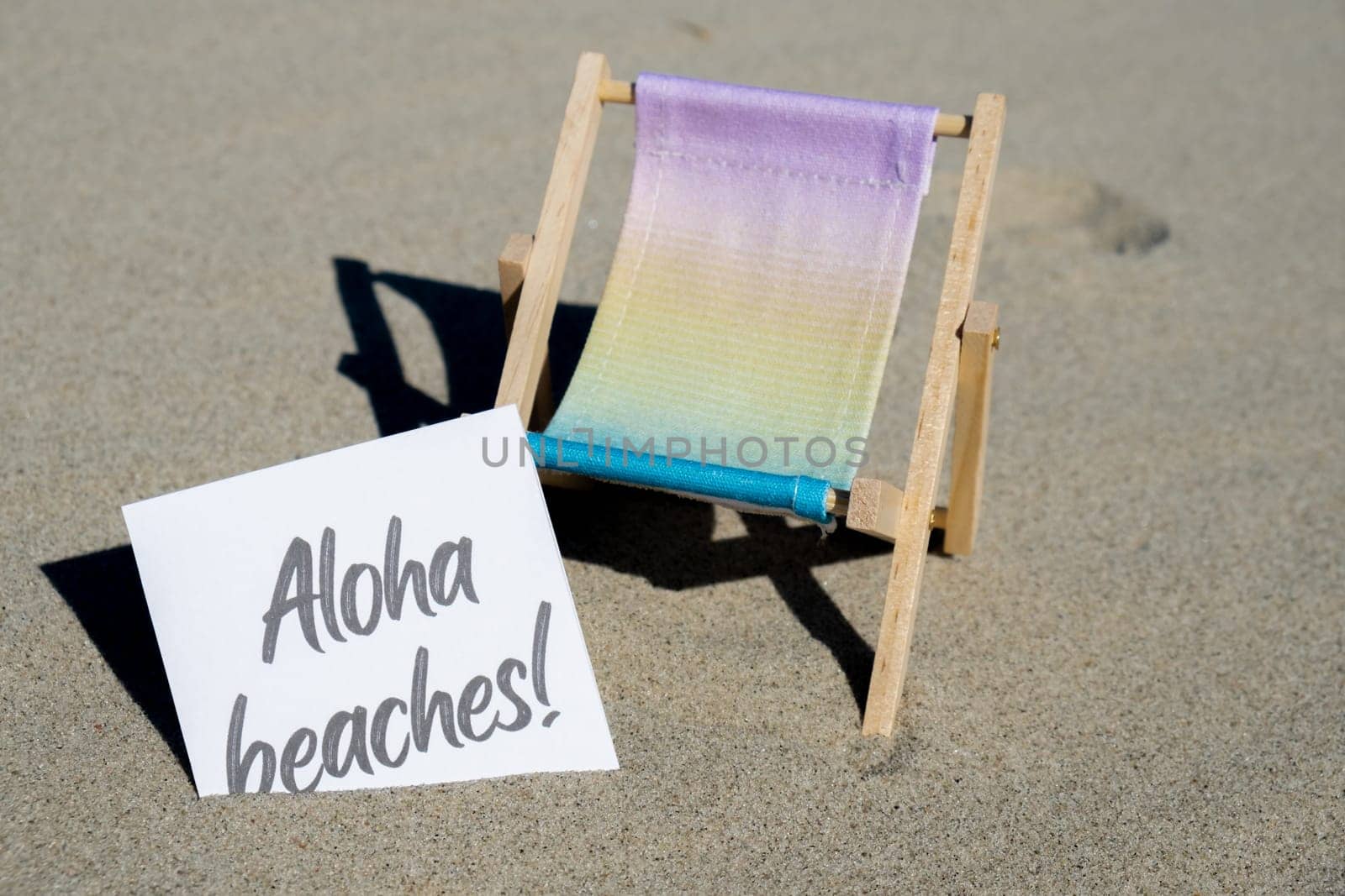 ALOHA BEACHES text on paper greeting card on background of beach chair lounge summer vacation decor. Sandy beach sun. Holiday concept postcard. Travel by anna_stasiia