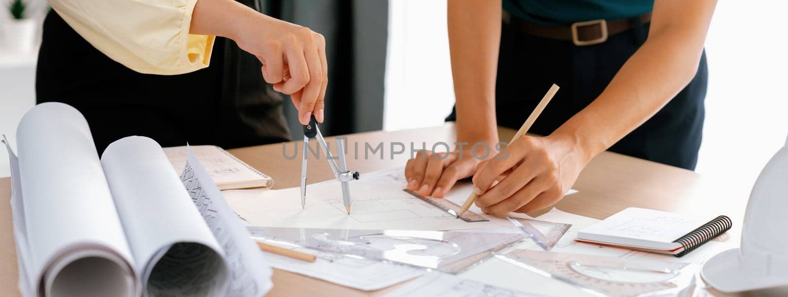 Professional architect team used divider measure during draft blueprint on table with architectural document, safety helmet and blueprint scatter around. Closeup. Focus on hand. Delineation.