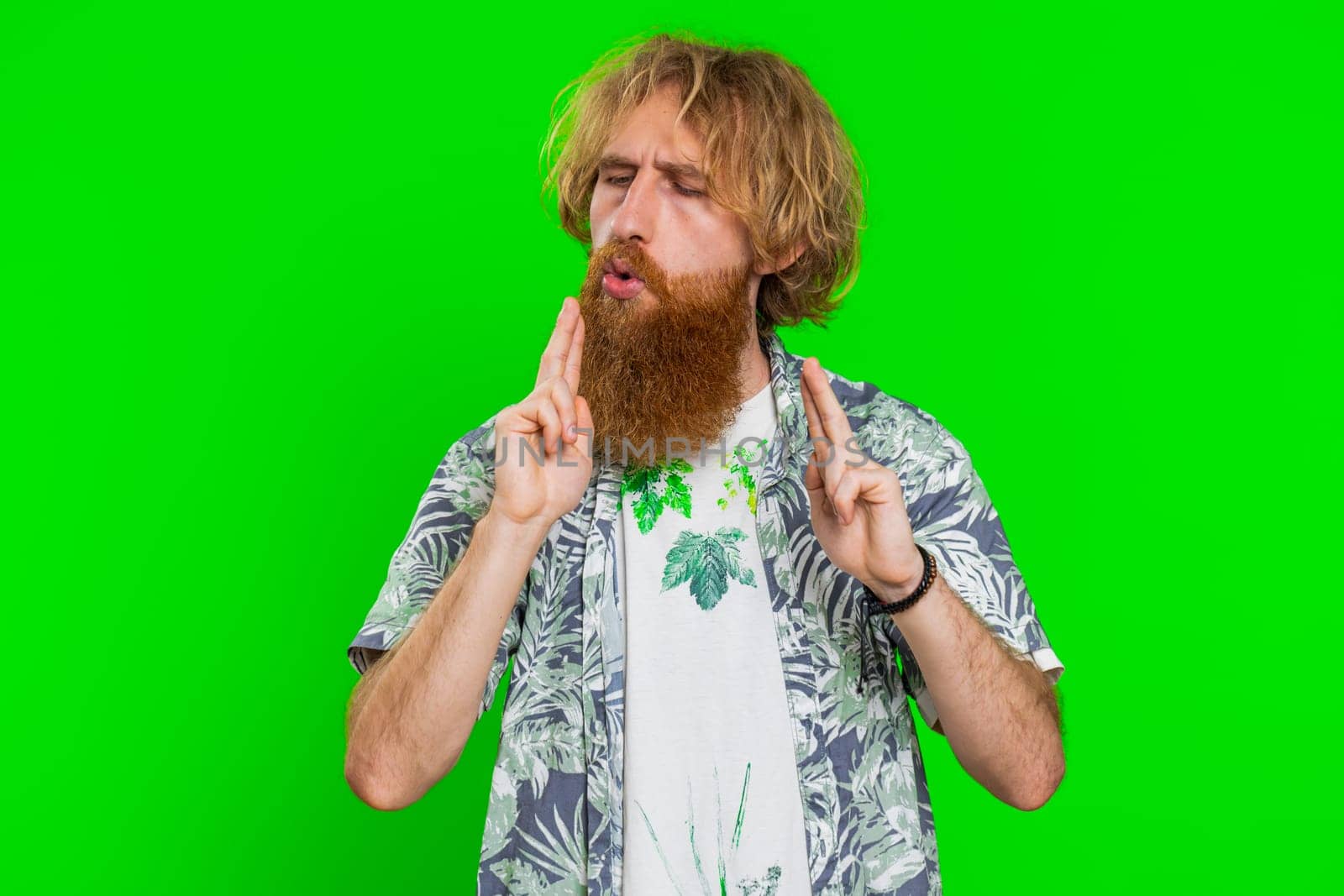 Young bearded man pointing around with finger gun gesture, looking confident making choice shooting killing with hand pistol right on target. Guy isolated on green chroma key background. Advertisement