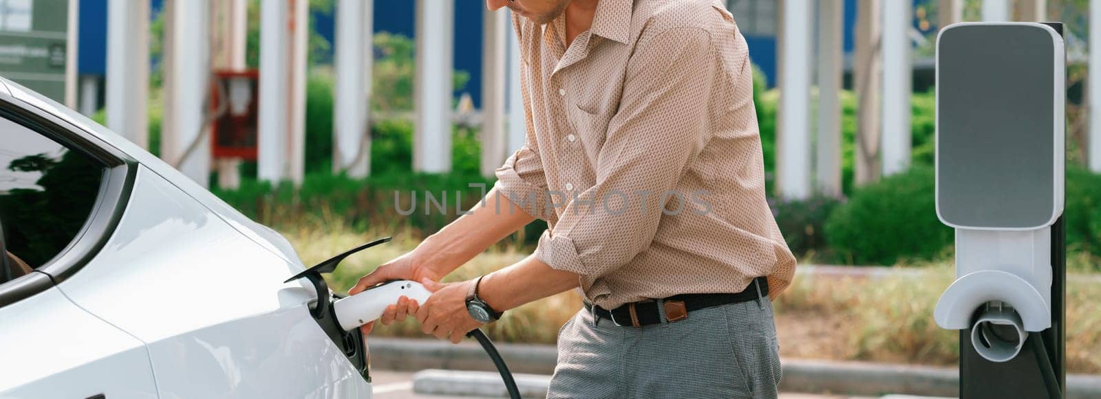 Young man recharge electric car's battery from charging station. Expedient by biancoblue