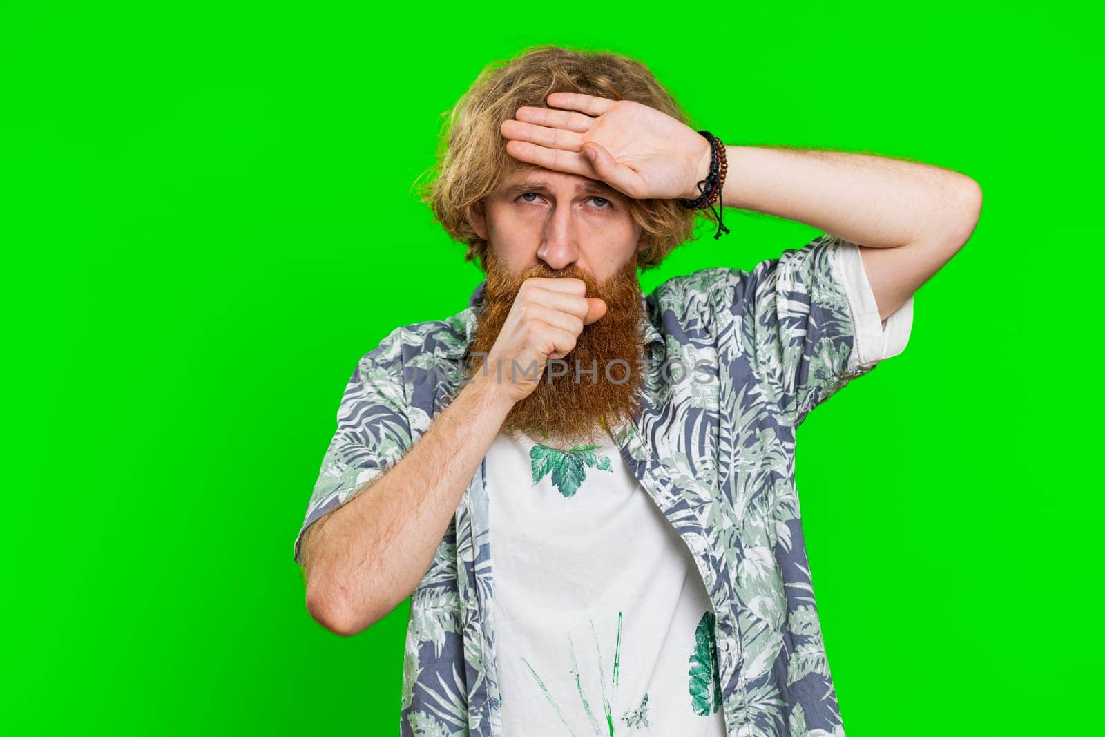 Unhealthy young caucasian man coughing with seasonal flu symptoms covering mouth with hand, feeling sick, allergy, fever or viral infection. Unwell ill guy isolated on green chroma key background