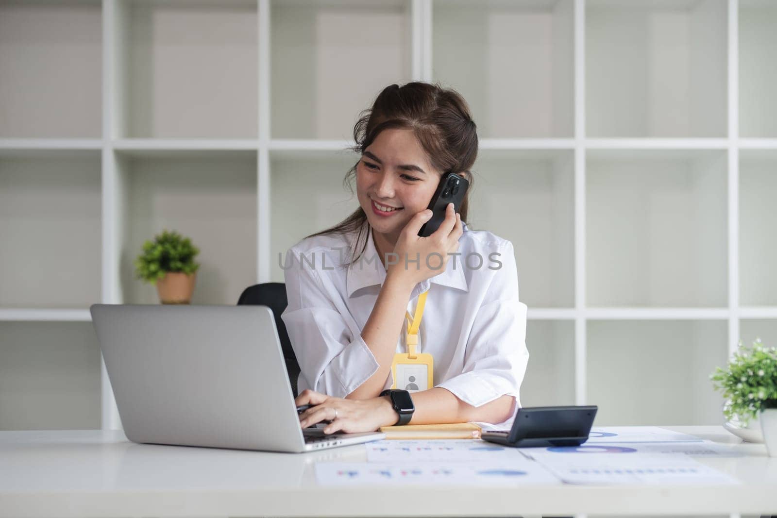 Business Caucasian woman Talking on the phone and using a laptop with a smile while sitting at modern office.