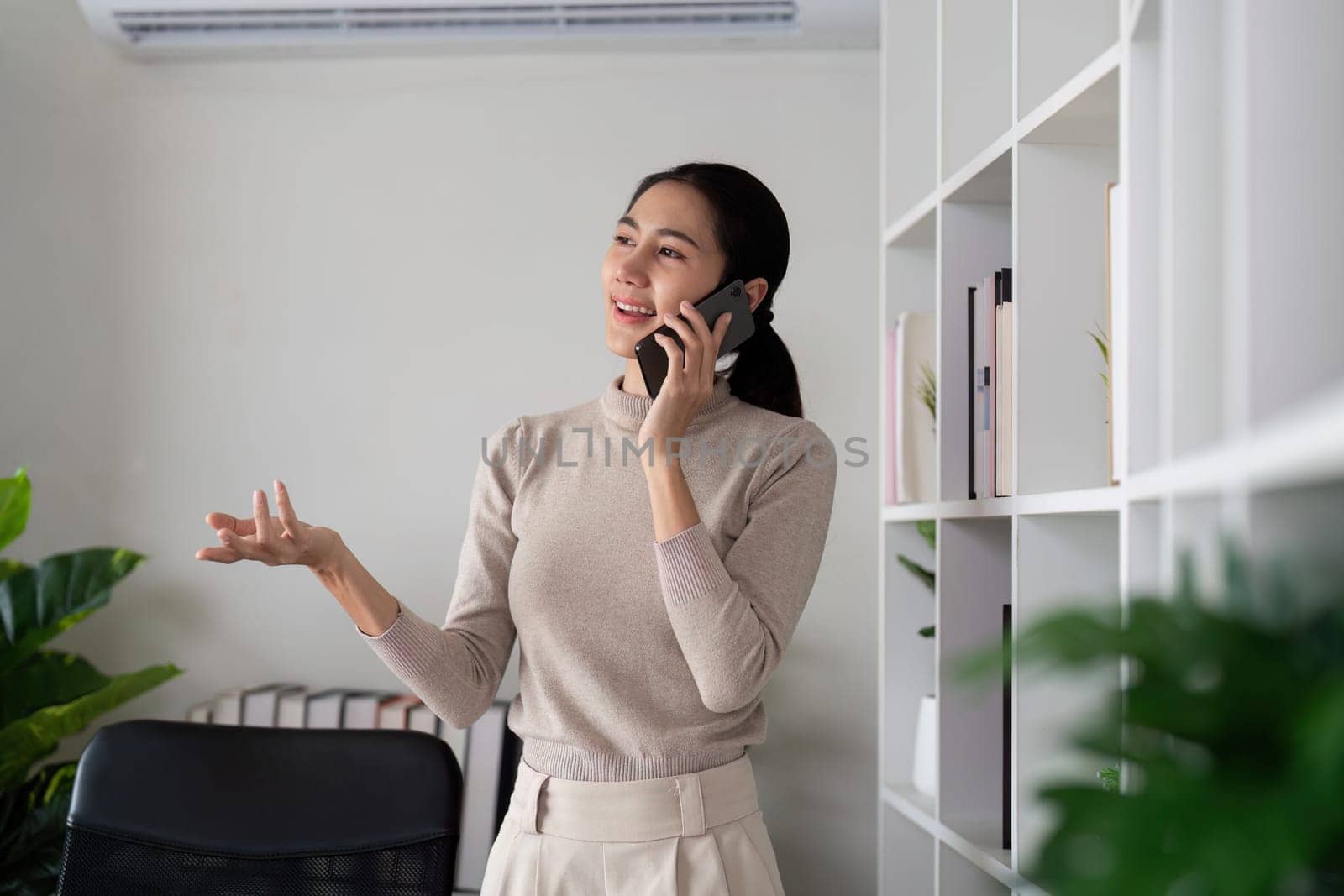 Successful businesswoman speaking by smartphone and smiling happily while standing in office.
