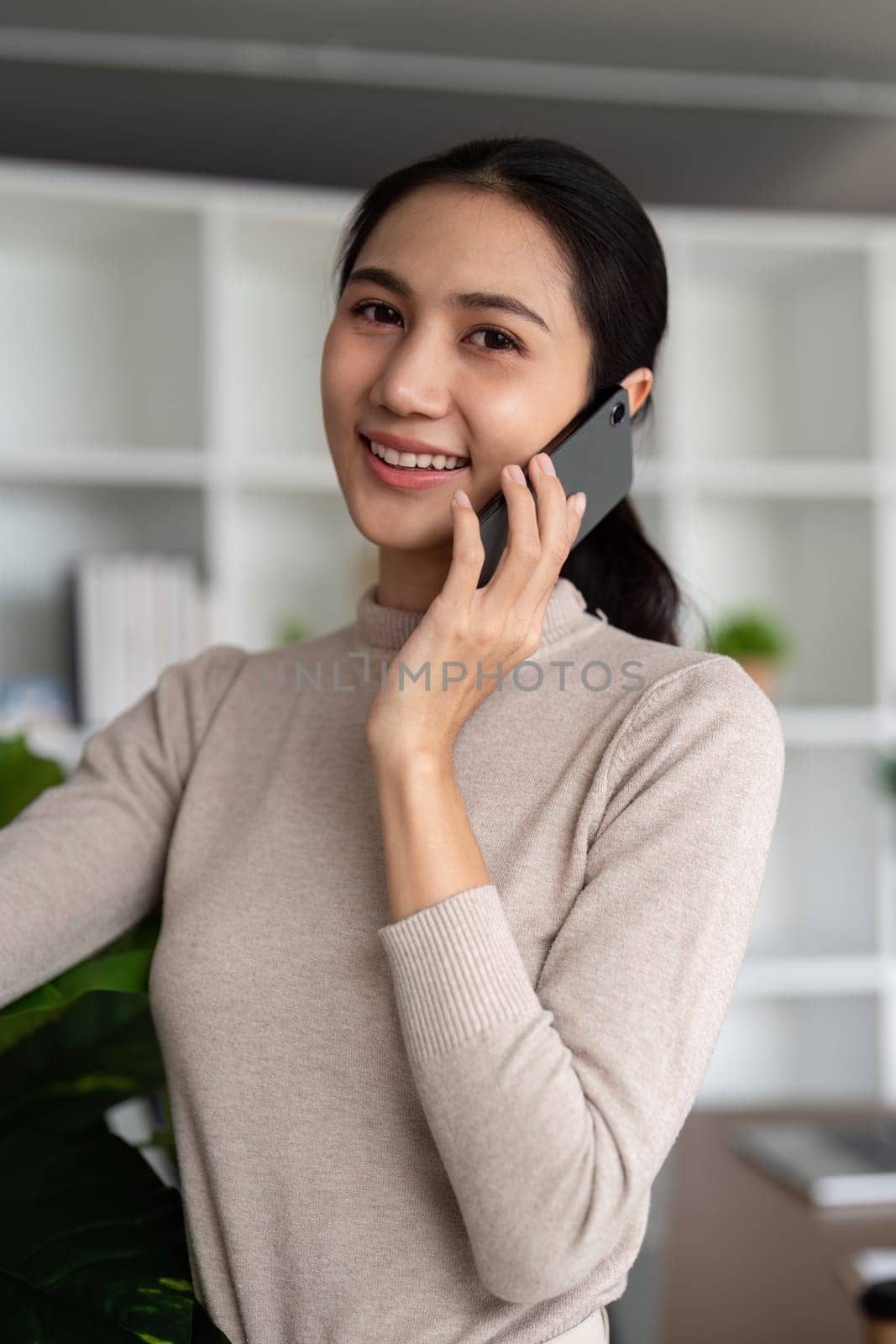 Successful businesswoman speaking by smartphone and smiling happily while standing in office.