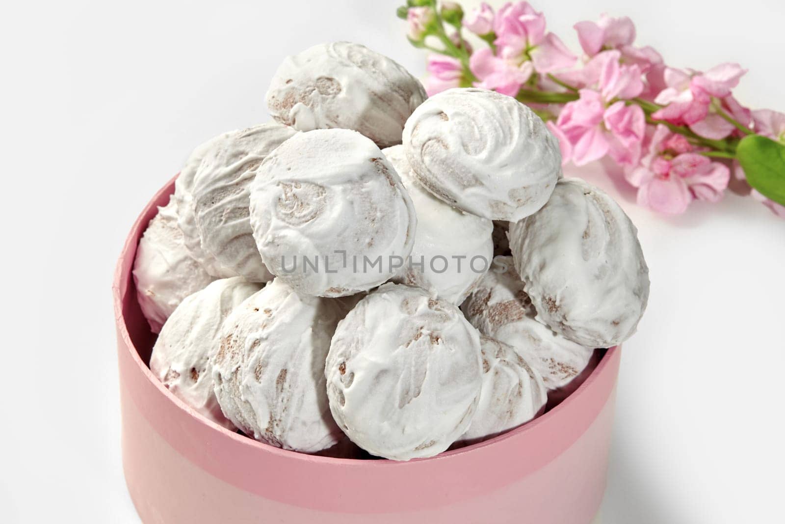 Heap of sugar glazed honey gingerbread cookies, presented in charming pink box with spring flowers in background. Traditional baked sweets