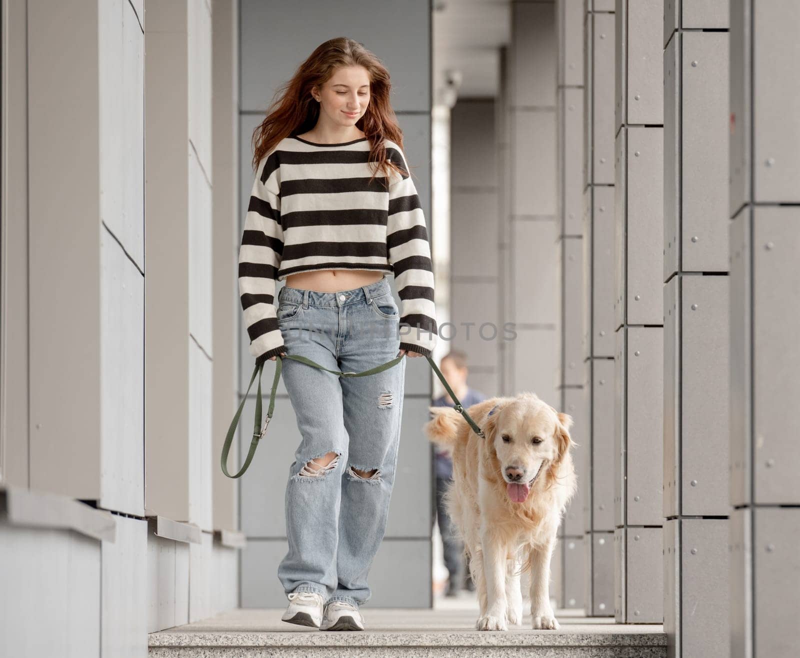 Teenage Girl Walks With Golden Retriever In City During Spring