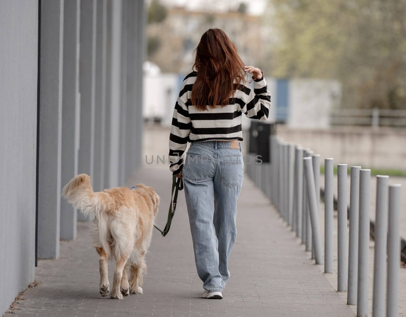 Teen Girl With Golden Retriever Sits In City During Spring, Viewed From Behind