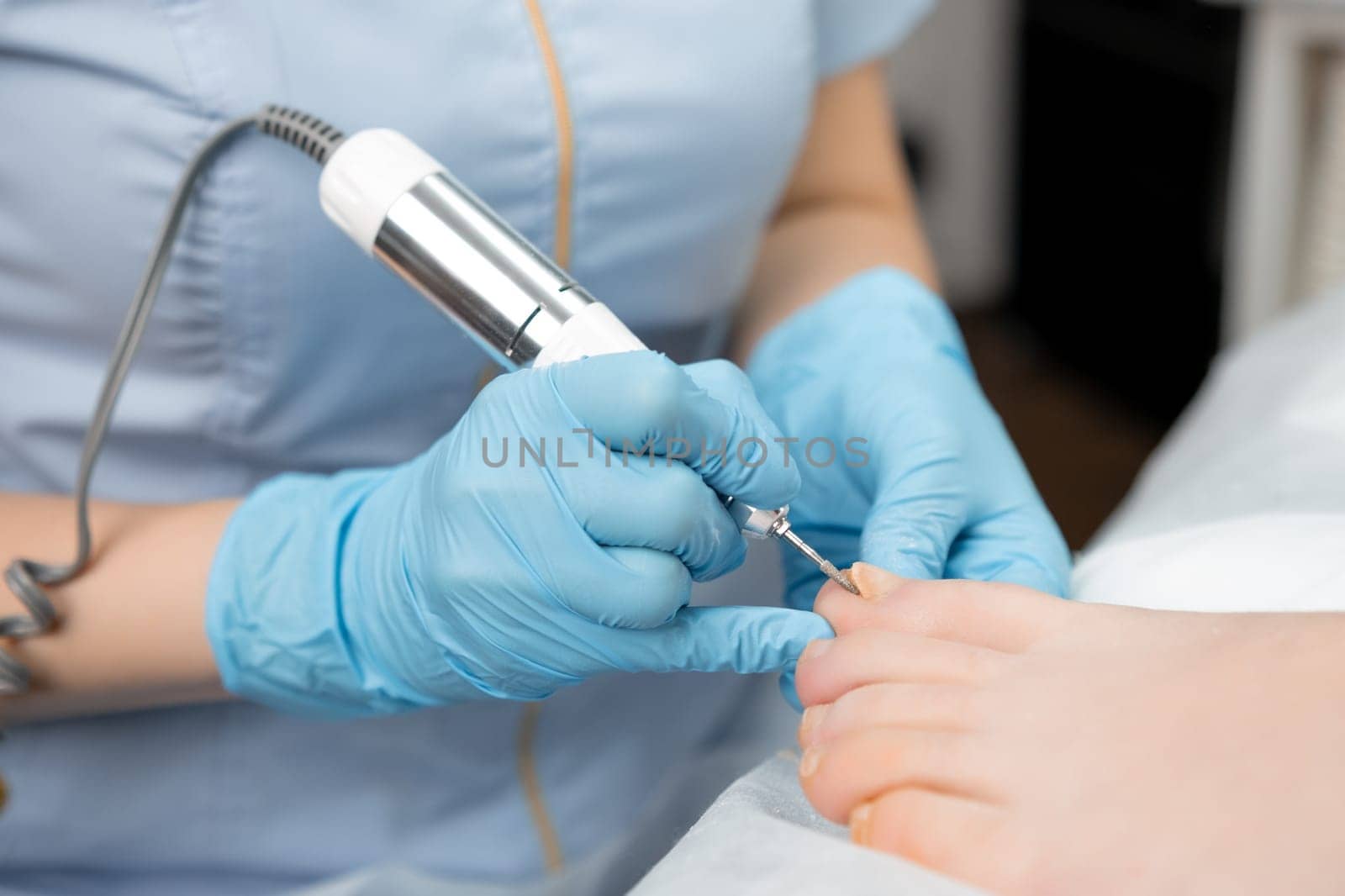 A master pedicurist provides a hardware pedicure to a woman, using a nail drill