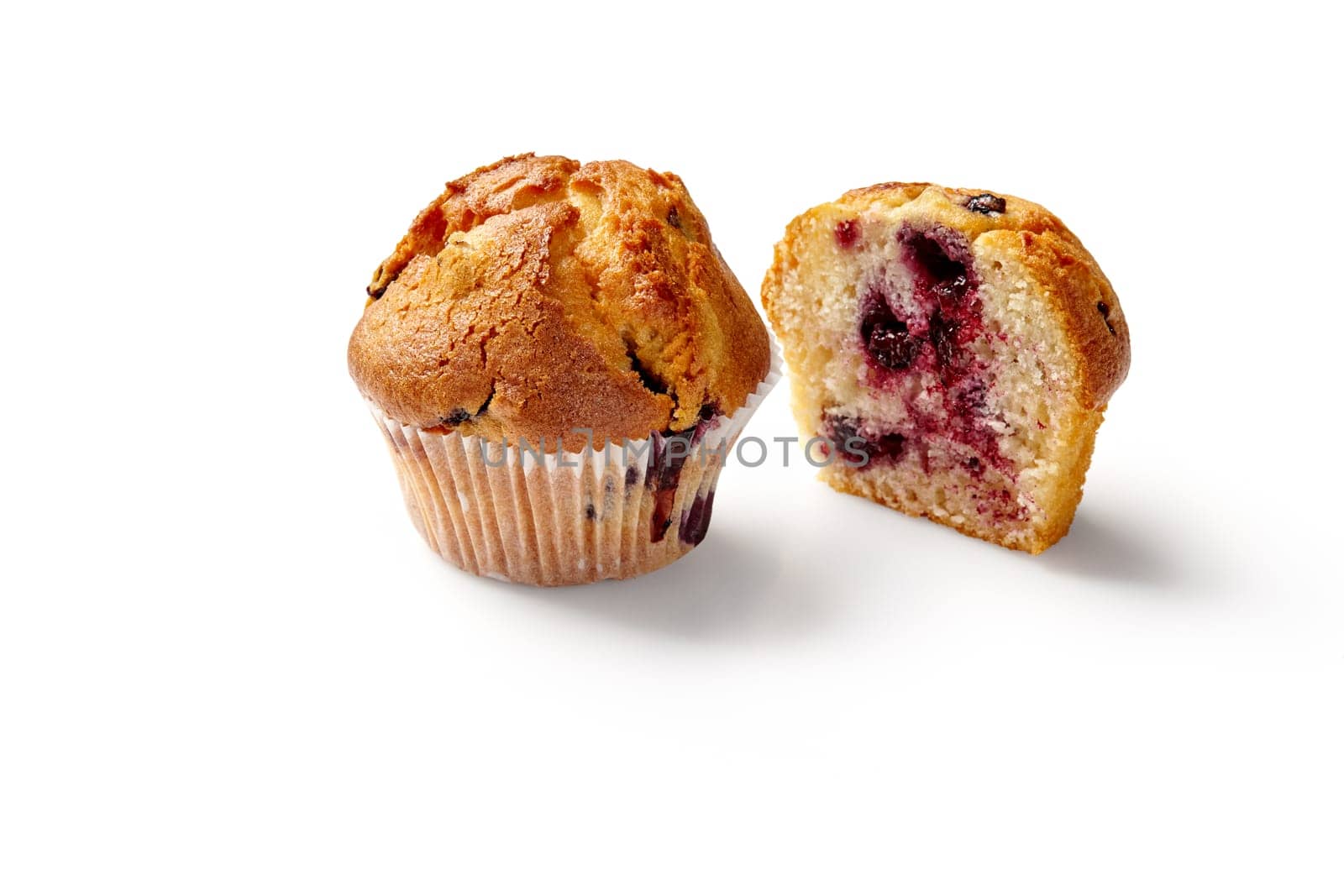Appetizing whole and sliced fluffy vanilla muffins with ripe currant filling in paper wrapper on white background. Popular baked desserts