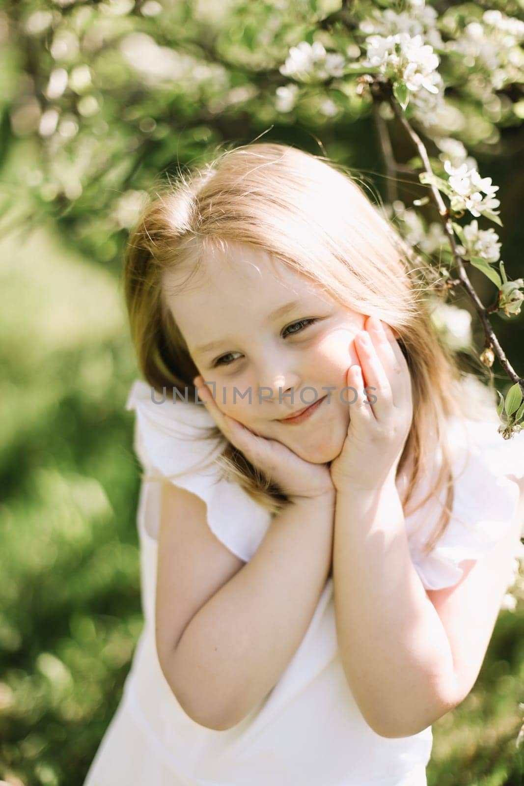 Portrait of little toddler girl in blossoming garden in spring. Cute beautiful lovely child having fun in a park on a sunny day. Happy smiling baby