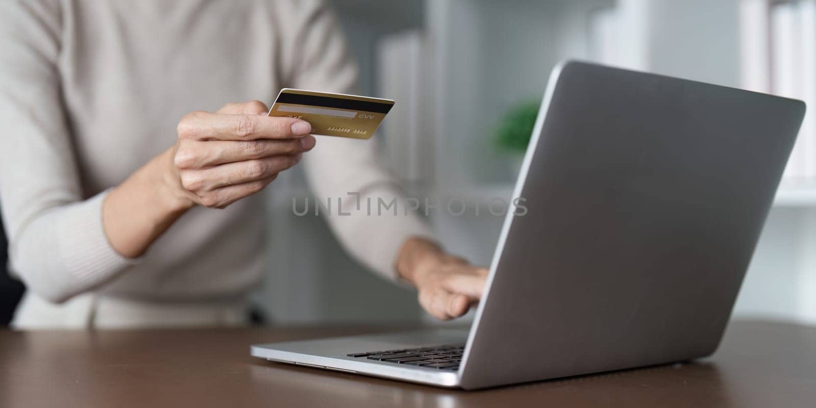 A woman is using a laptop to pay for something with a credit card. She is holding the card in her hand and typing on the keyboard. Concept of convenience and ease