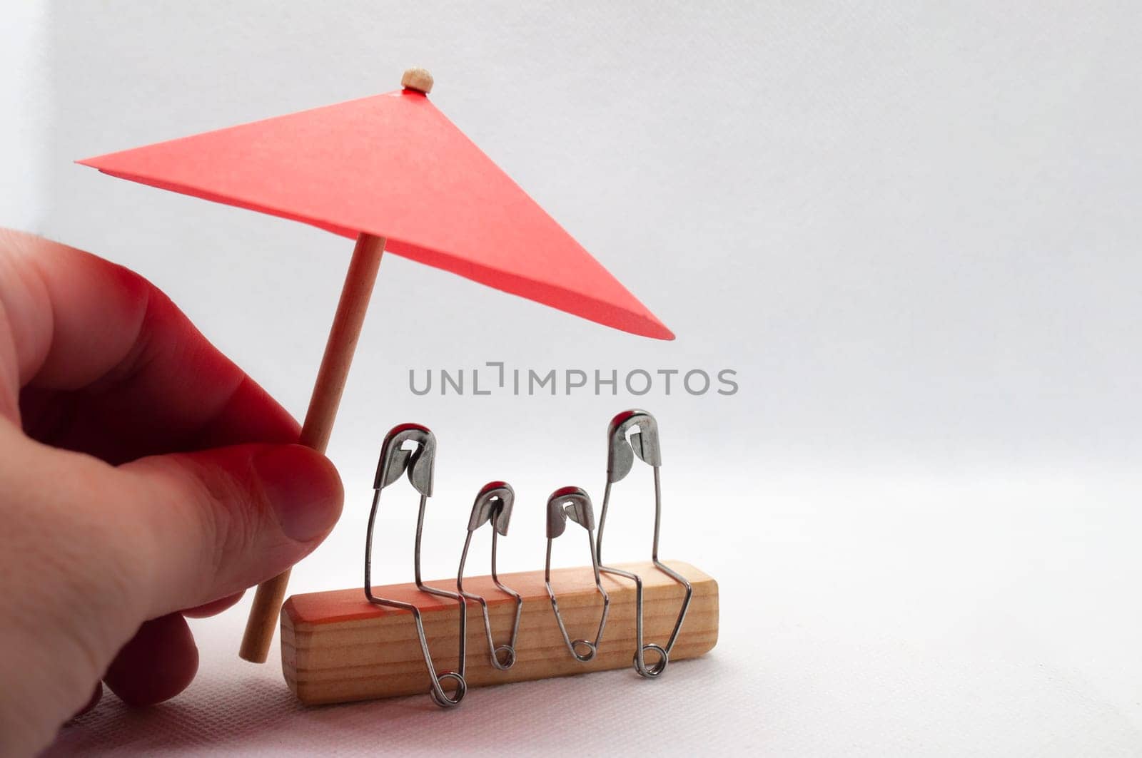 Model safety pin of family sitting on wooden block with red umbrella background. Insurance concept.