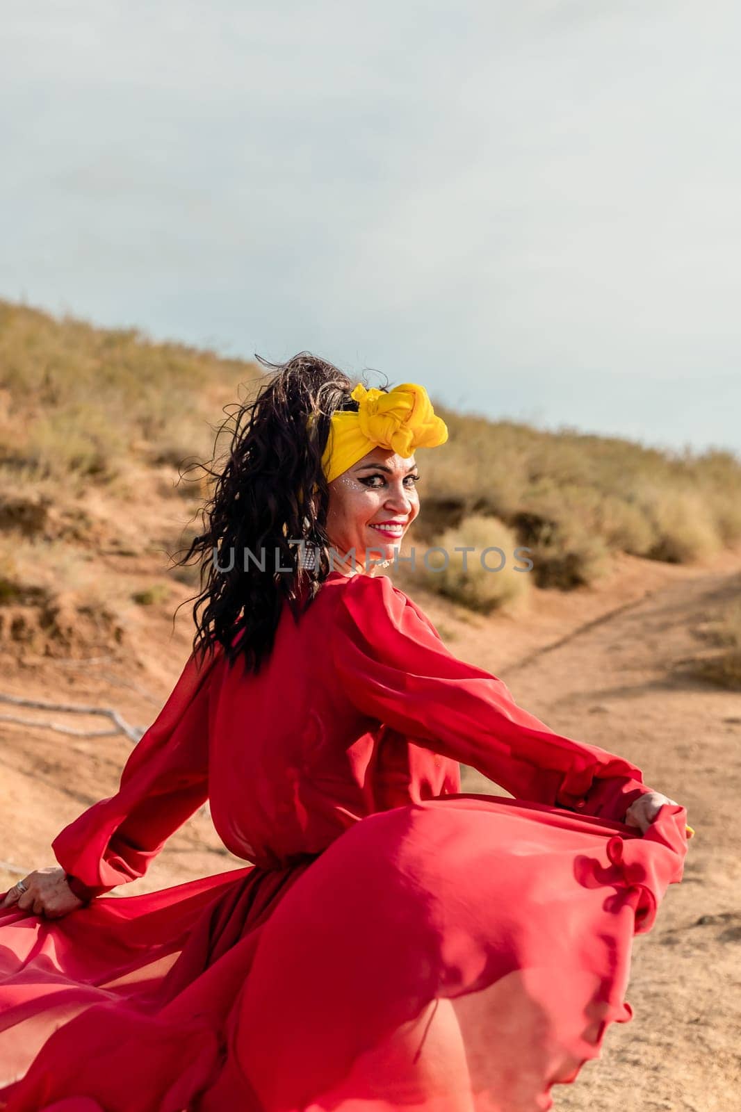 A woman in a red dress and yellow headband is walking on a dirt path. She is smiling and she is happy