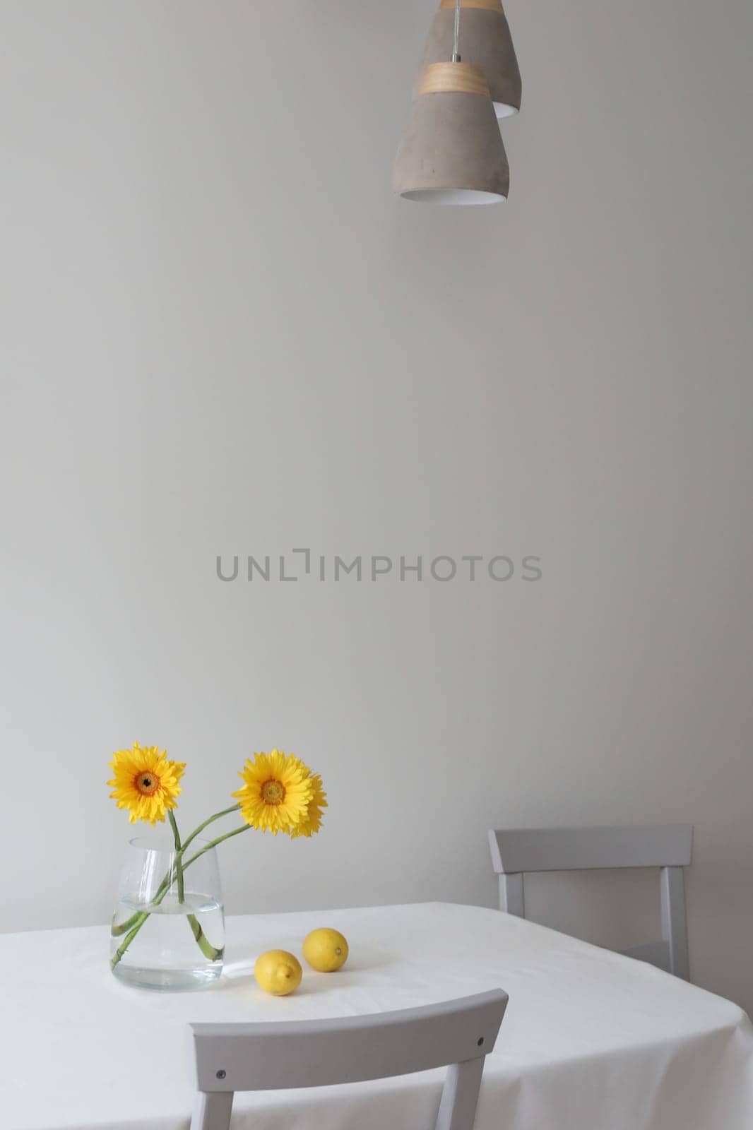 still life with lemons and yellow gerberas in a glass jar on a table covered with linen tablecloth. Summer composition with lemons and yellow flowers on kitchen table. by paralisart