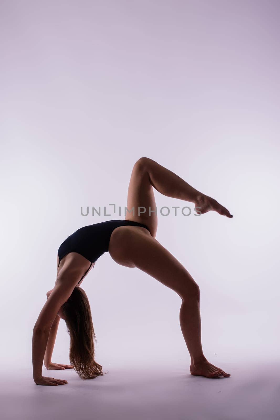 Athletic, beautiful, young girl with sportive strong body training in bodysuit against orange studio background. Flexibility. Concept of sport, healthy and active lifestyle, beauty, fitness.