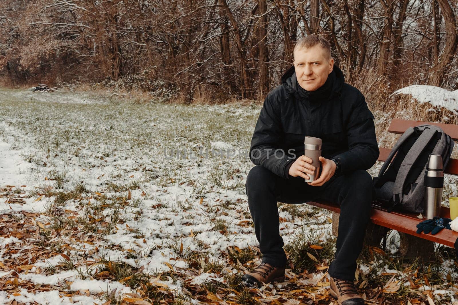Winter Serenity: 40-Year-Old Man Enjoying Tea on Snow-Covered Bench in Rural Park. Immerse yourself in the tranquil beauty of winter as a 40-year-old man finds solace on a snowy bench in a rural park. Sipping hot tea from a thermos, he embraces the serene ambiance, surrounded by the peaceful, snow-covered nature. This captivating image captures the essence of winter leisure, offering a moment of seasonal joy and quiet contemplation amidst the breathtaking scenery.